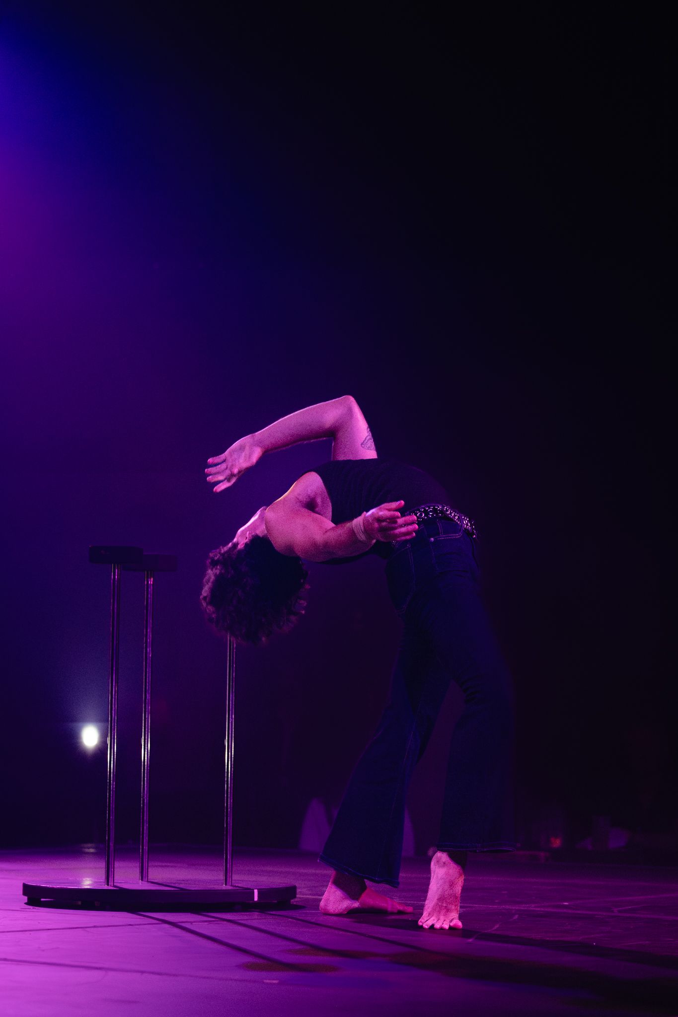 Contemporary dancer performs fluid movement sequence under dramatic purple lighting on dark stage.
