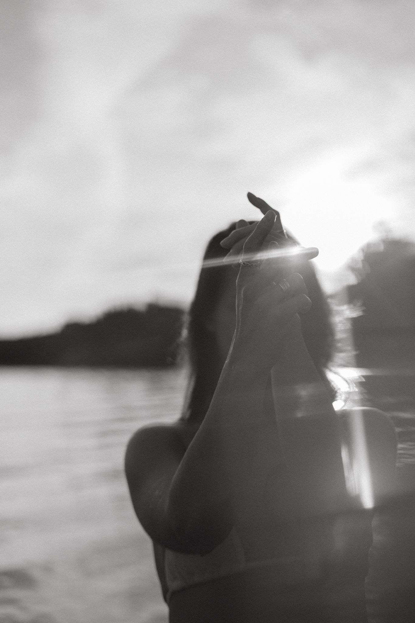 Monochrome silhouette of someone making expressive gestures by the water in dreamy backlit scenery.
