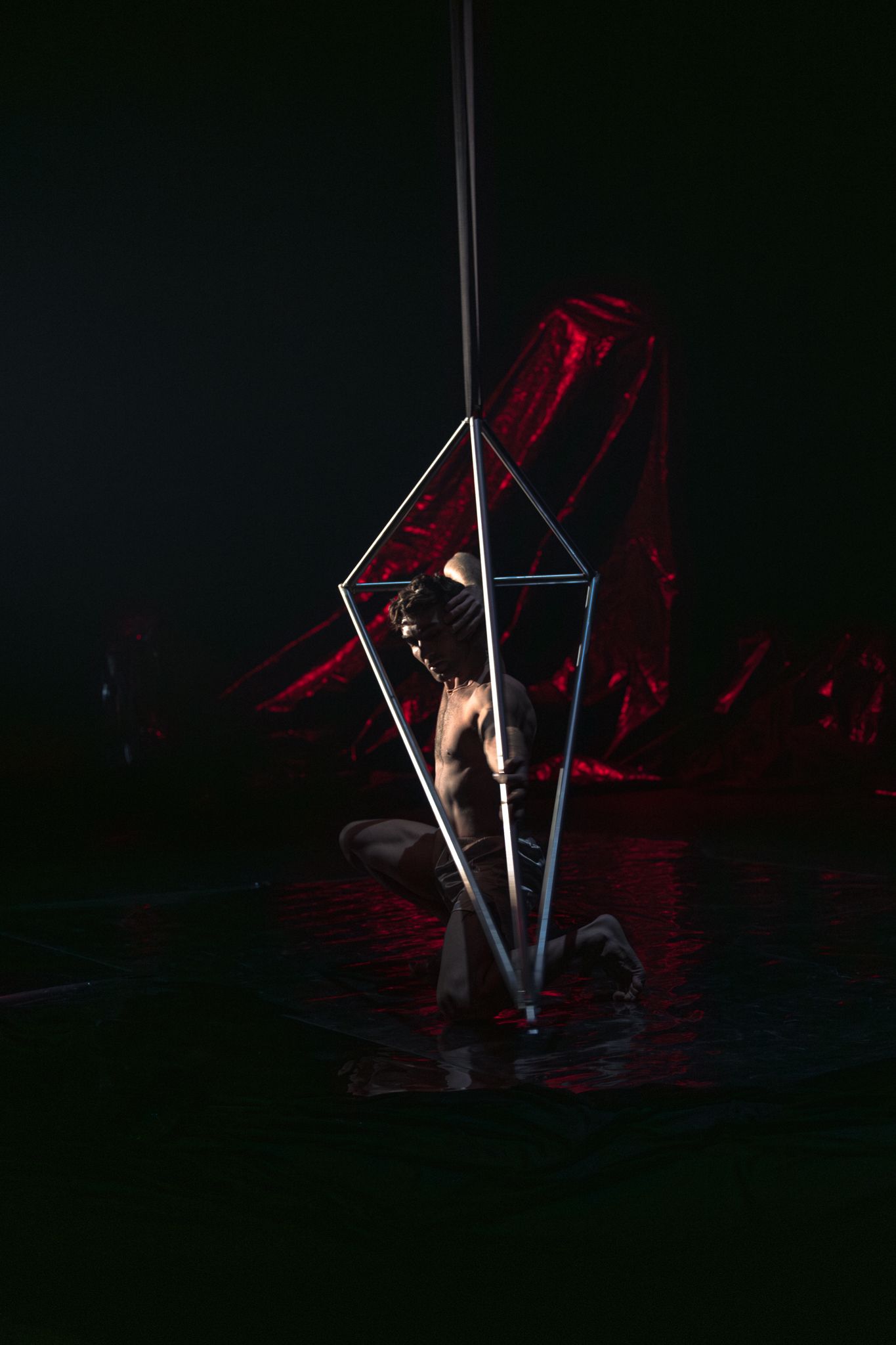 Artistic performance featuring illuminated poles against a dark backdrop with red lighting effects.