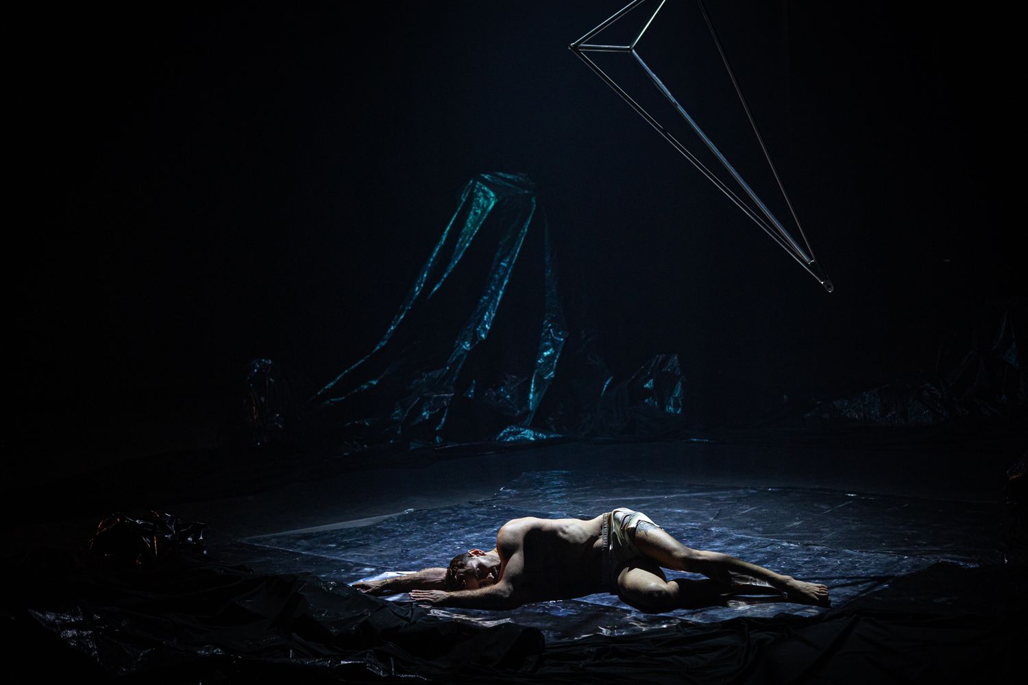 A dark and moody stage performance shows figures in dramatic lighting creating a haunting theatrical scene.