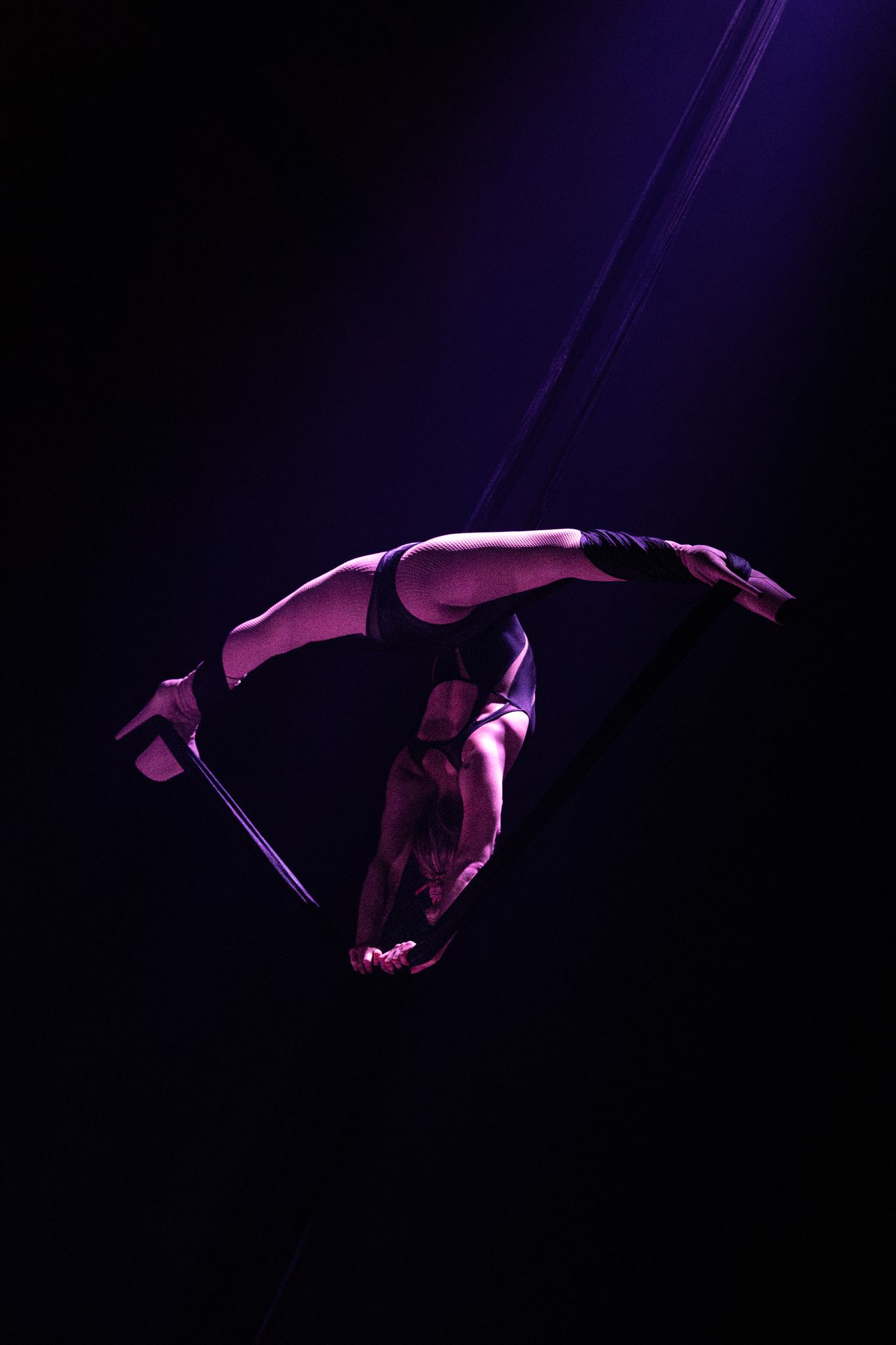 Acrobatic performer executes an impressive aerial flip in dramatic purple lighting on dark stage.