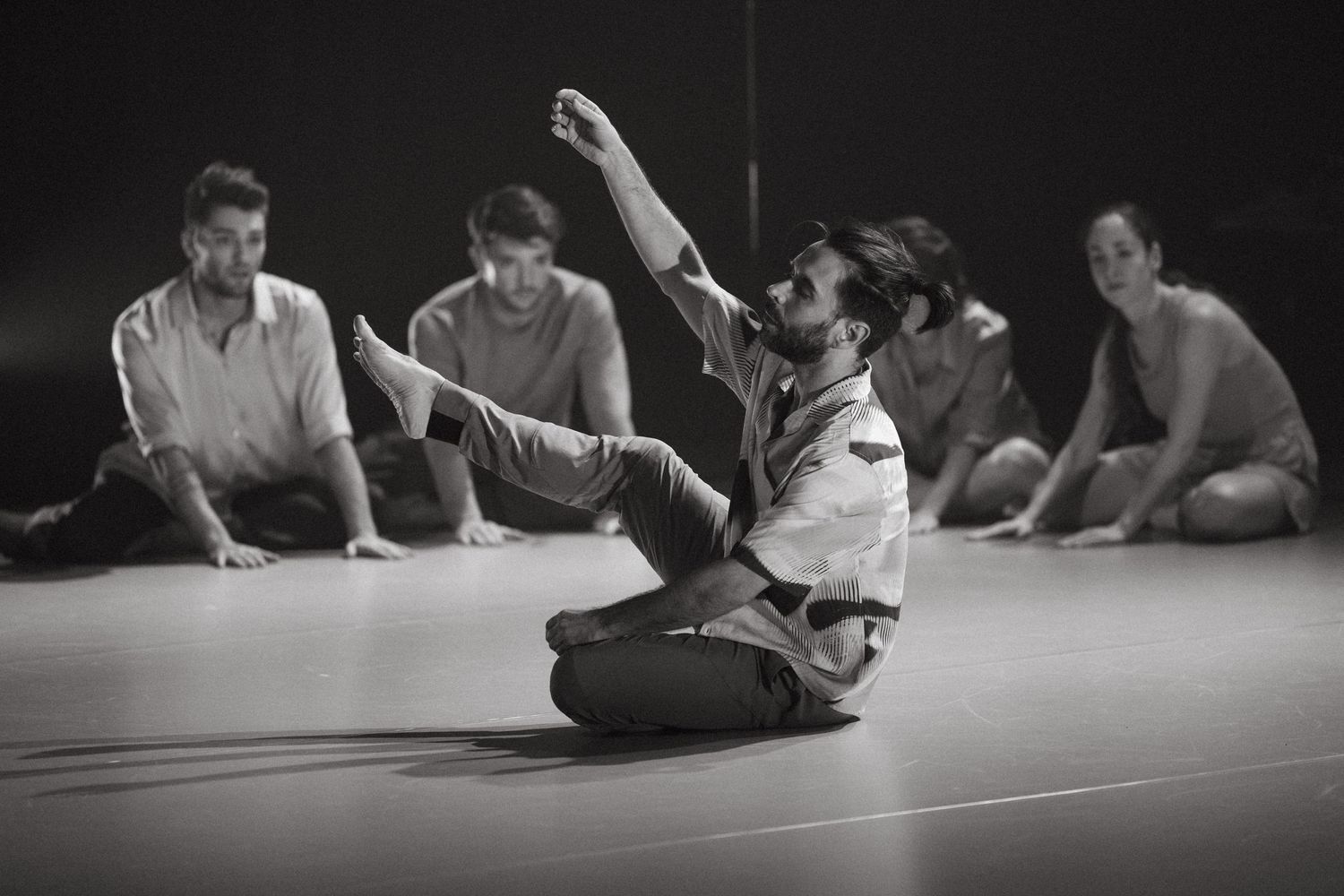 A graceful dance rehearsal scene captured in black and white showing performers on the floor in a studio.