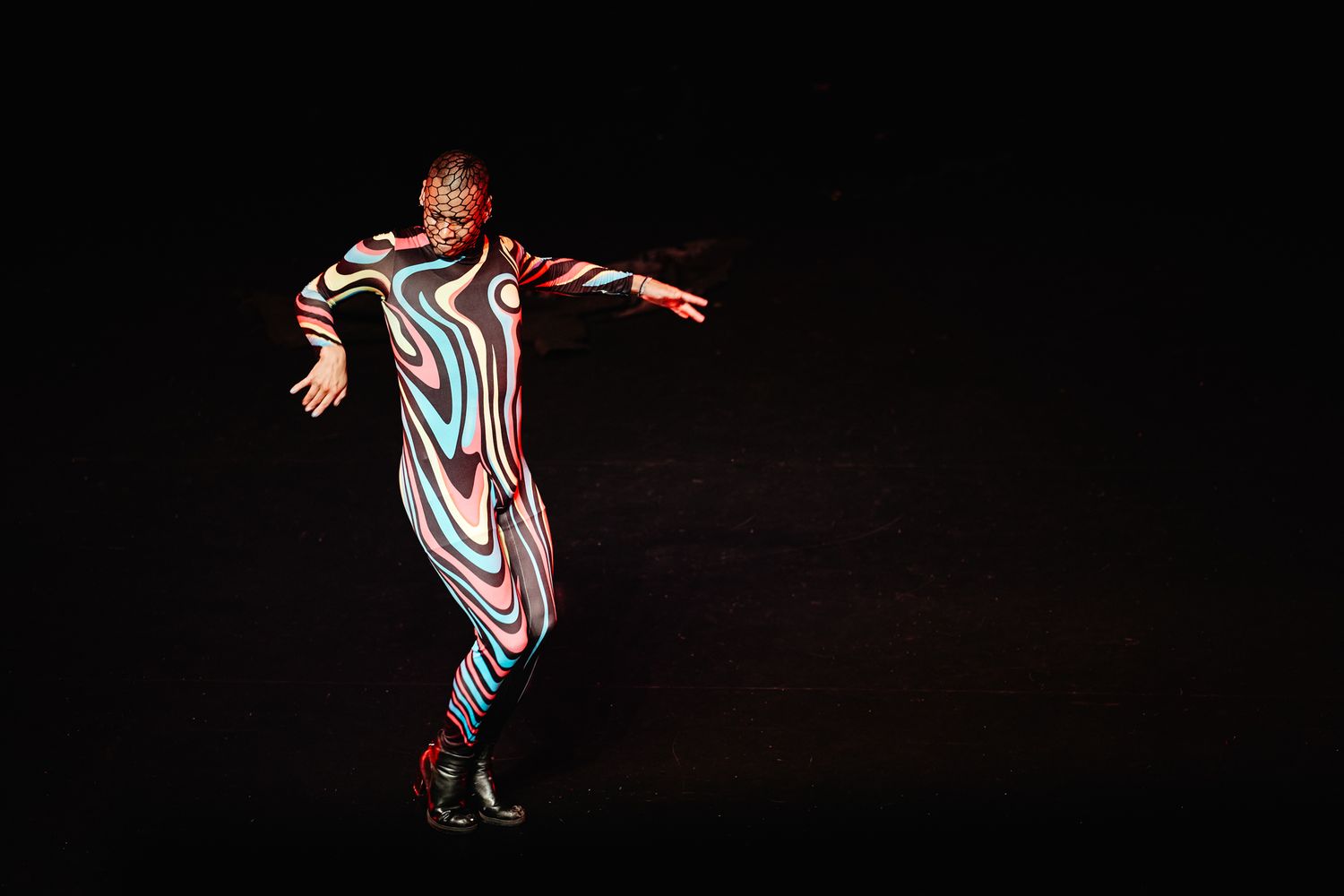 A performer in a striped bodysuit dances expressively on a dark stage with dramatic lighting.