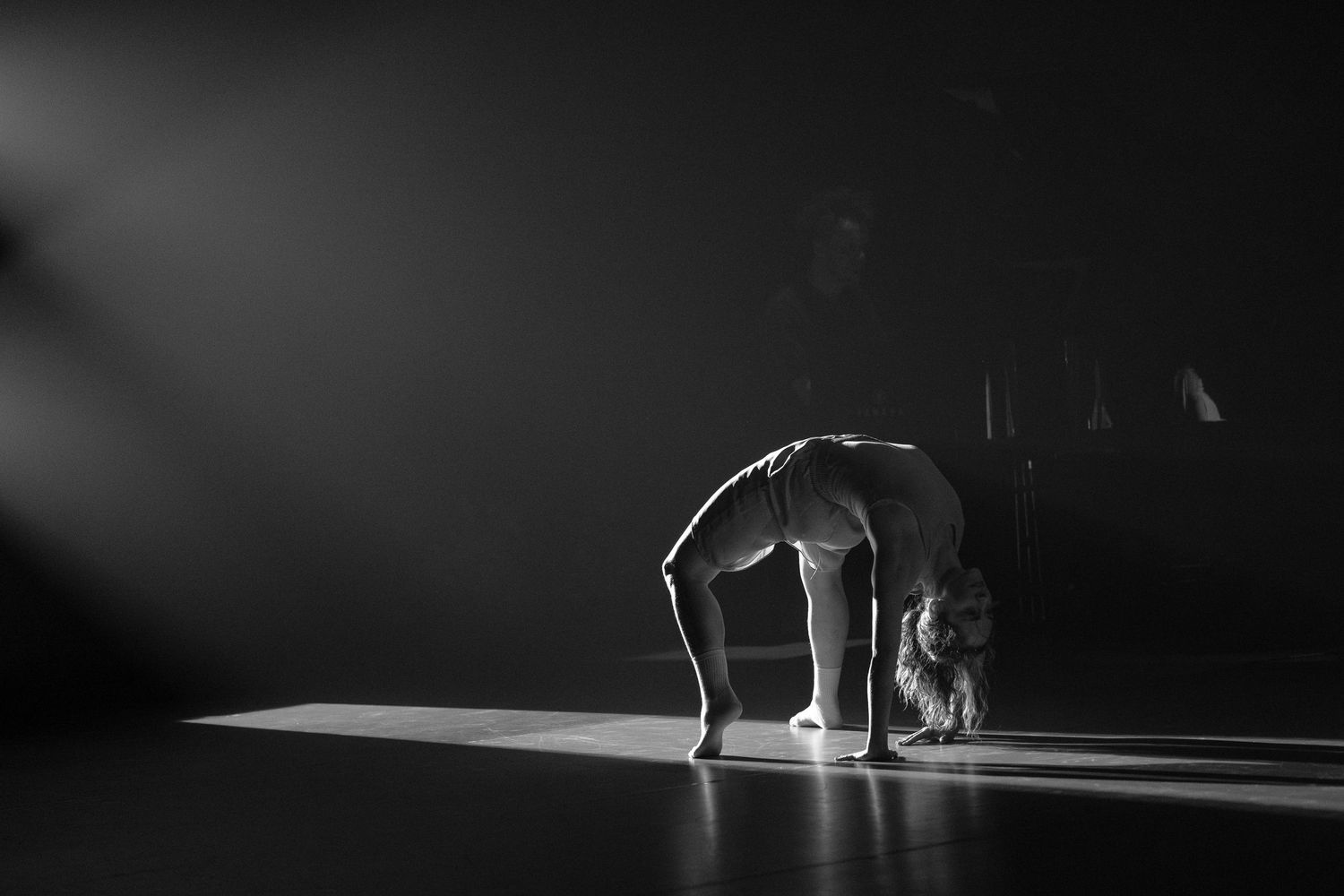 A dancer performs a backbend in dramatic lighting on a dark stage, captured in black and white photography.