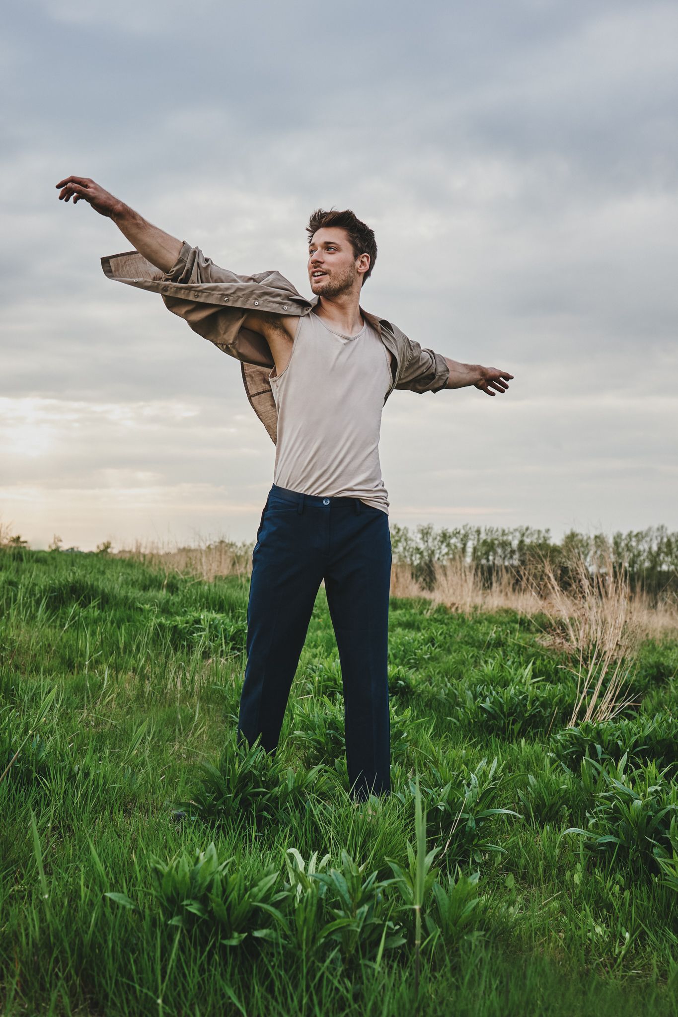 Figure dances freely in a green meadow while wearing casual clothing under cloudy skies.