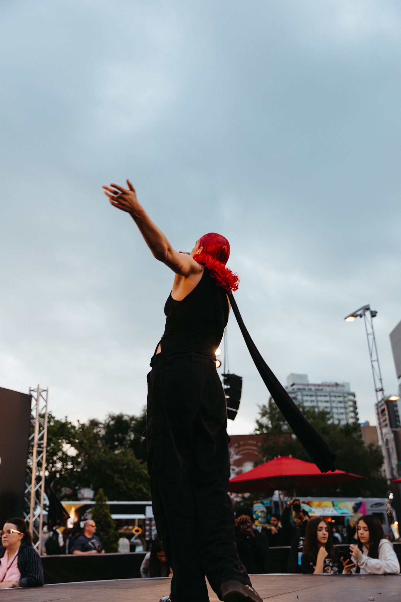 Dancers in red caps and dark outfits perform a dynamic outdoor movement sequence against a cloudy sky.