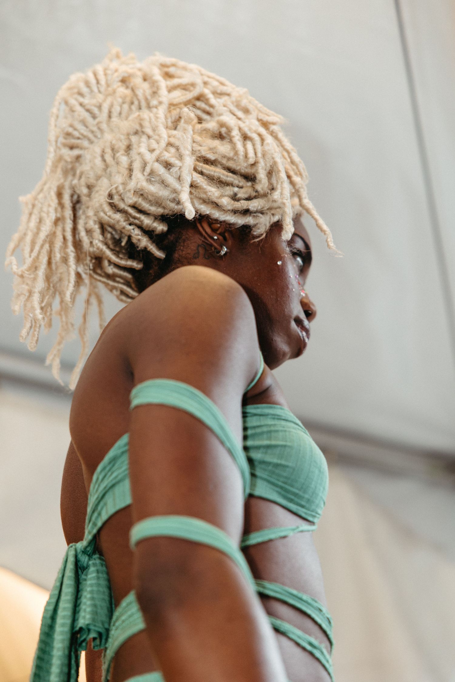 Side profile portrait showing platinum blonde dreadlocks and mint green wrapped fabric against a light background.