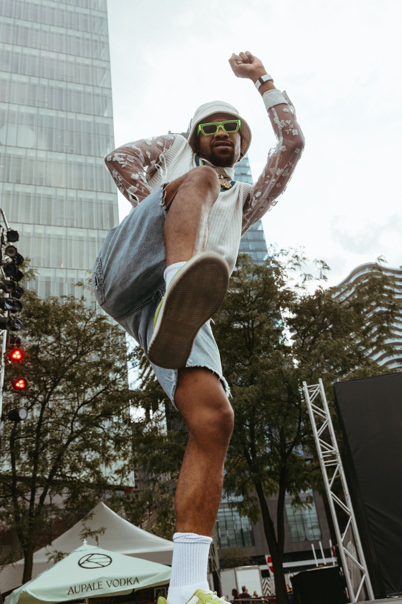 A performer dances energetically on an outdoor stage at an urban event with office buildings visible in the background.