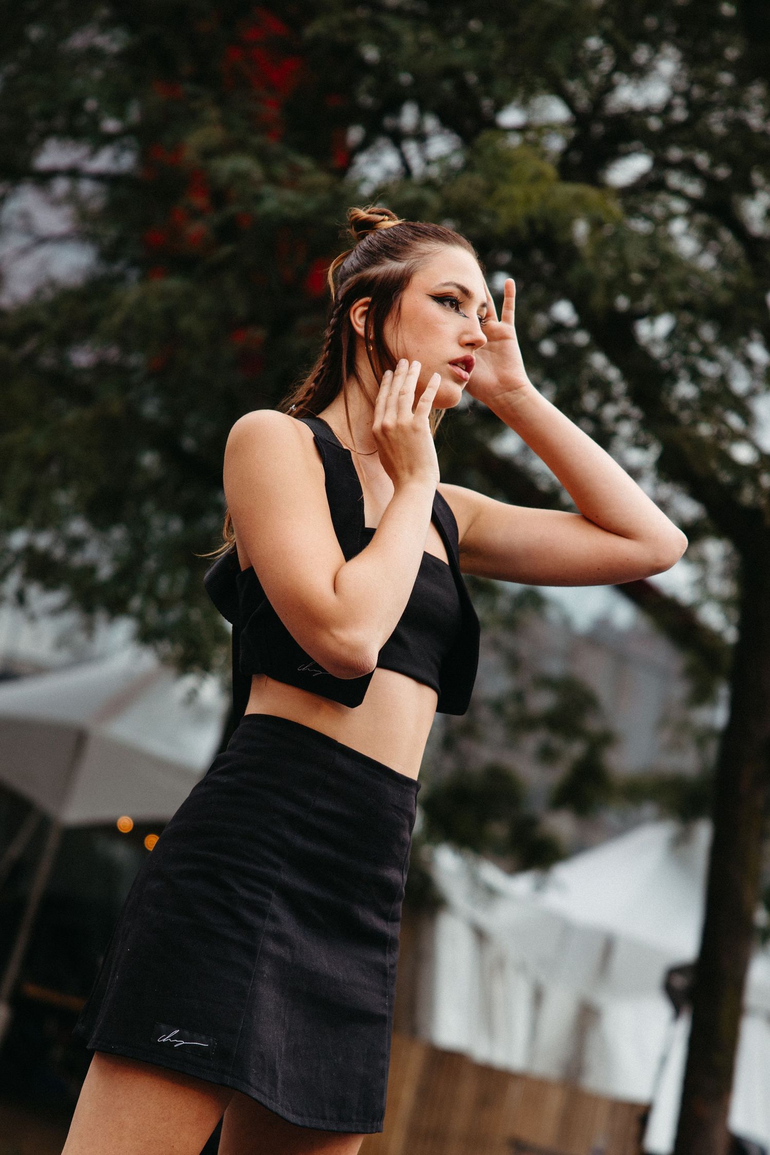 Athletic woman in black crop top and skirt poses outdoors with dramatic expression against blurred natural background.