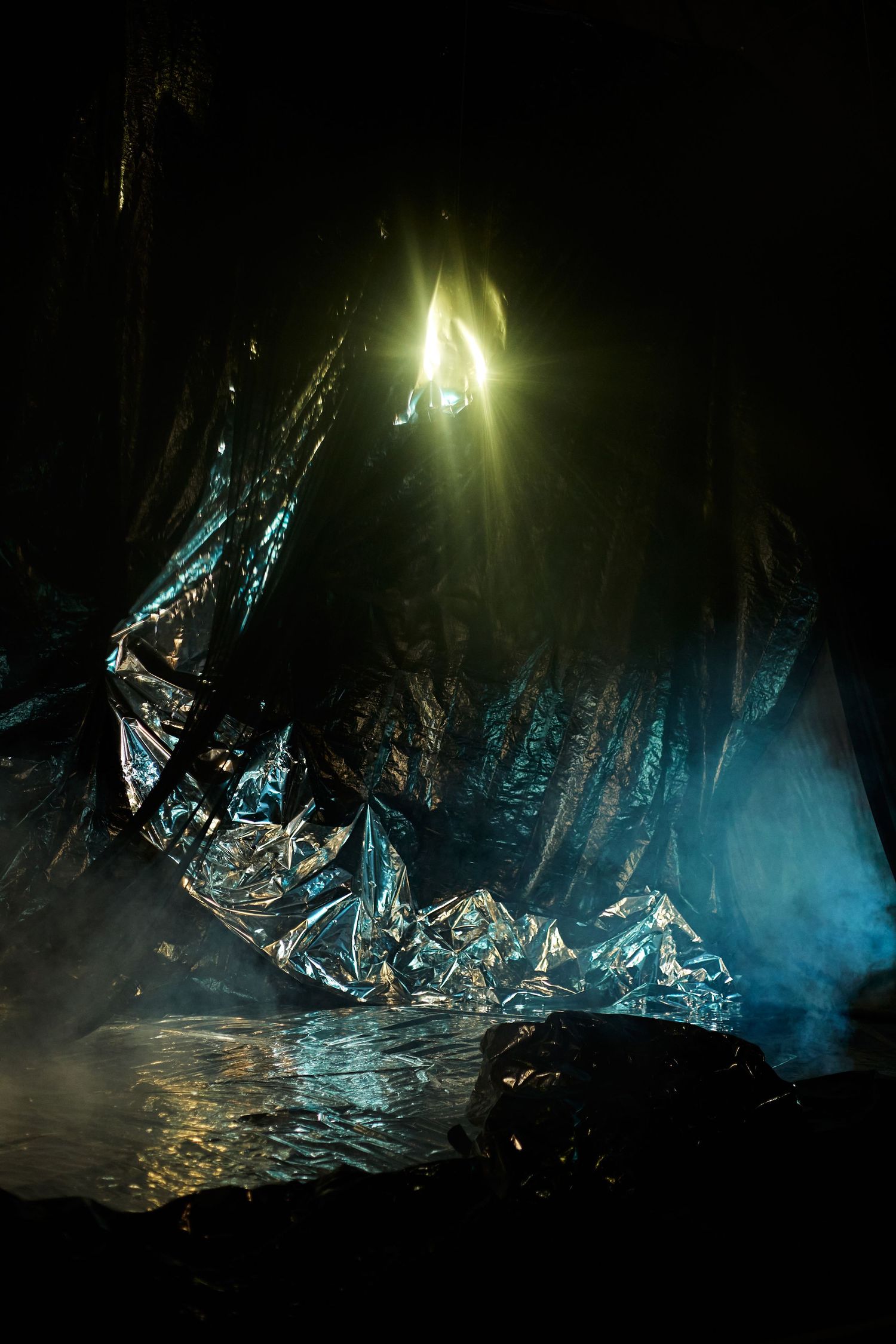 Dramatic cave interior with shimmering metallic formations illuminated by bright light and cast in ethereal blue tones.