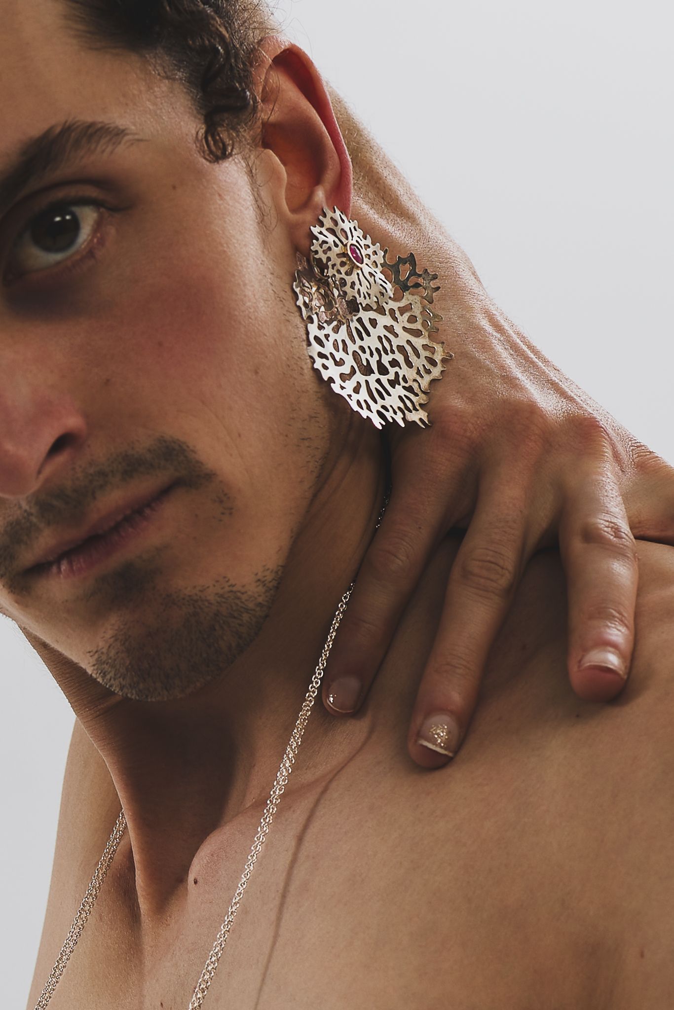 Artistic portrait highlighting an intricate silver filigree earring and delicate chain necklace against white background.