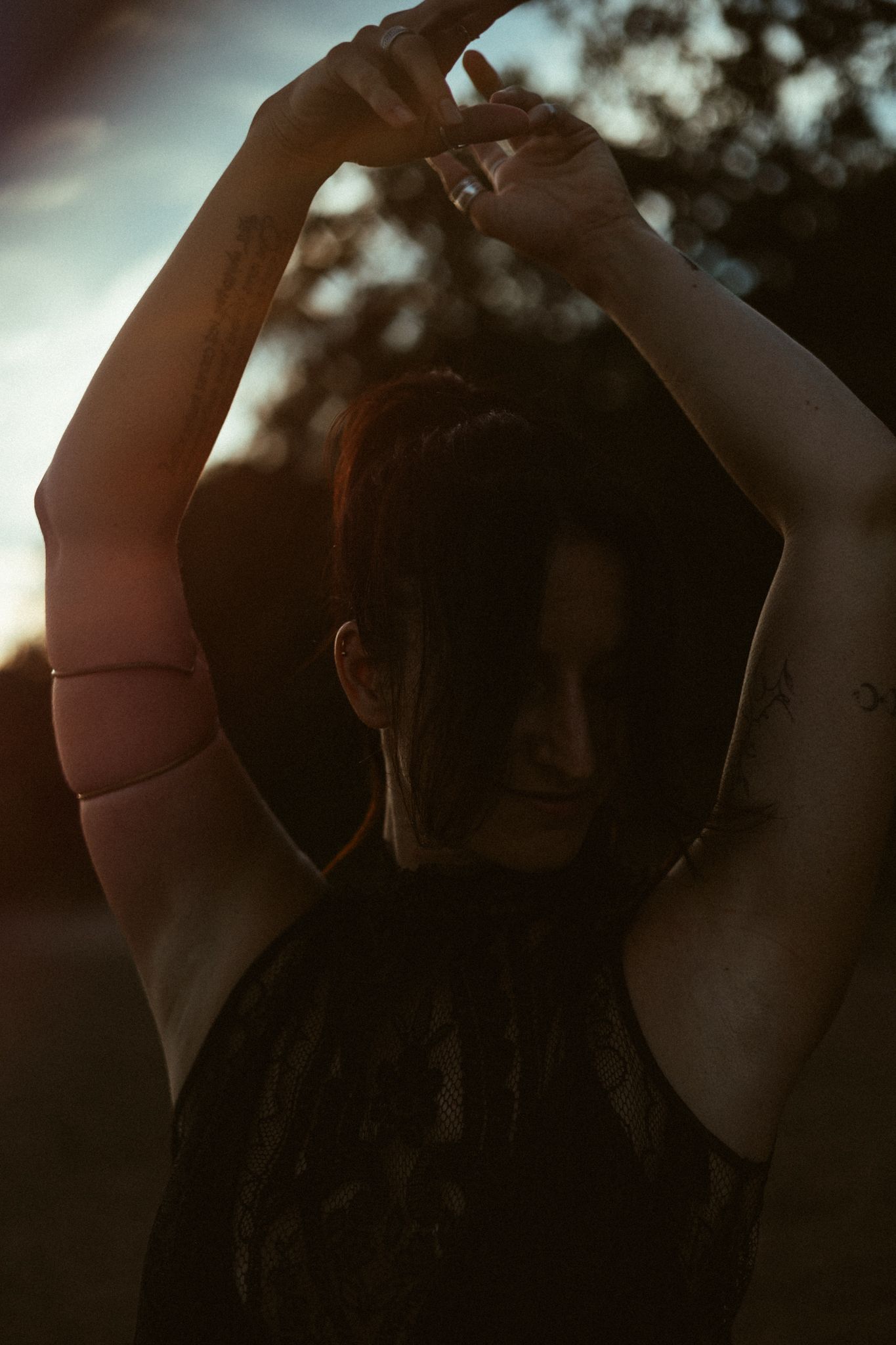 Silhouetted figure stretches arms overhead against moody sunset sky in artistic portrait.