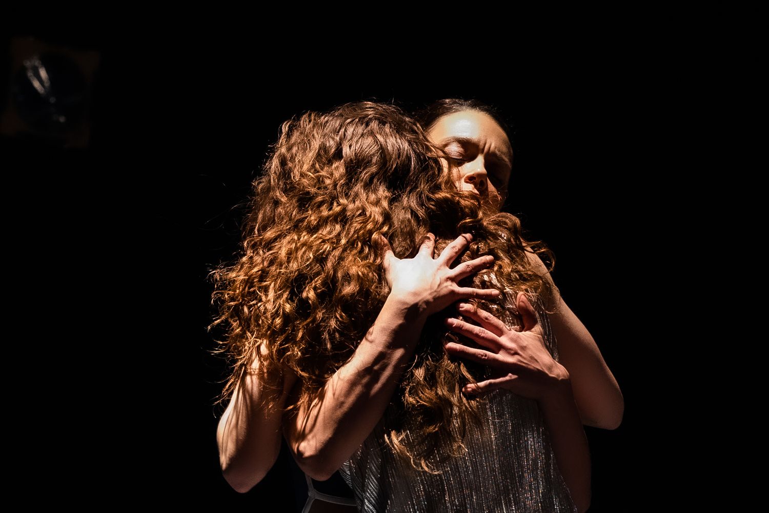 Two performers engaged in an emotional dance duet against a dark background with dramatic lighting.
