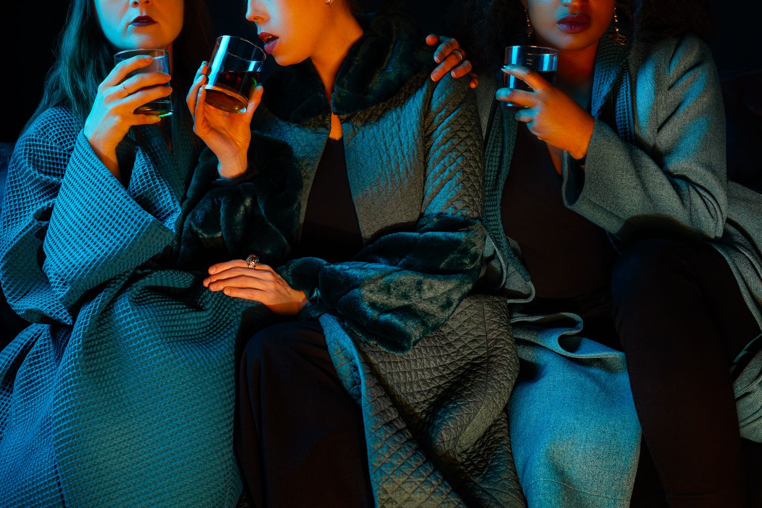 People in cozy sweaters holding drinks in a dimly lit room with dramatic blue lighting.
