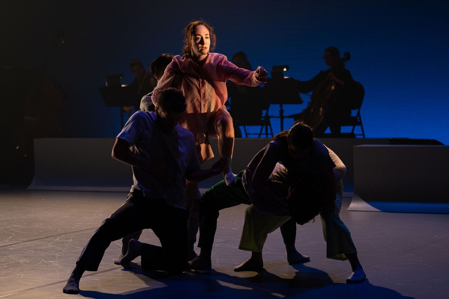 Dramatic sequence of two performers executing a contemporary dance lift against a dark blue background.