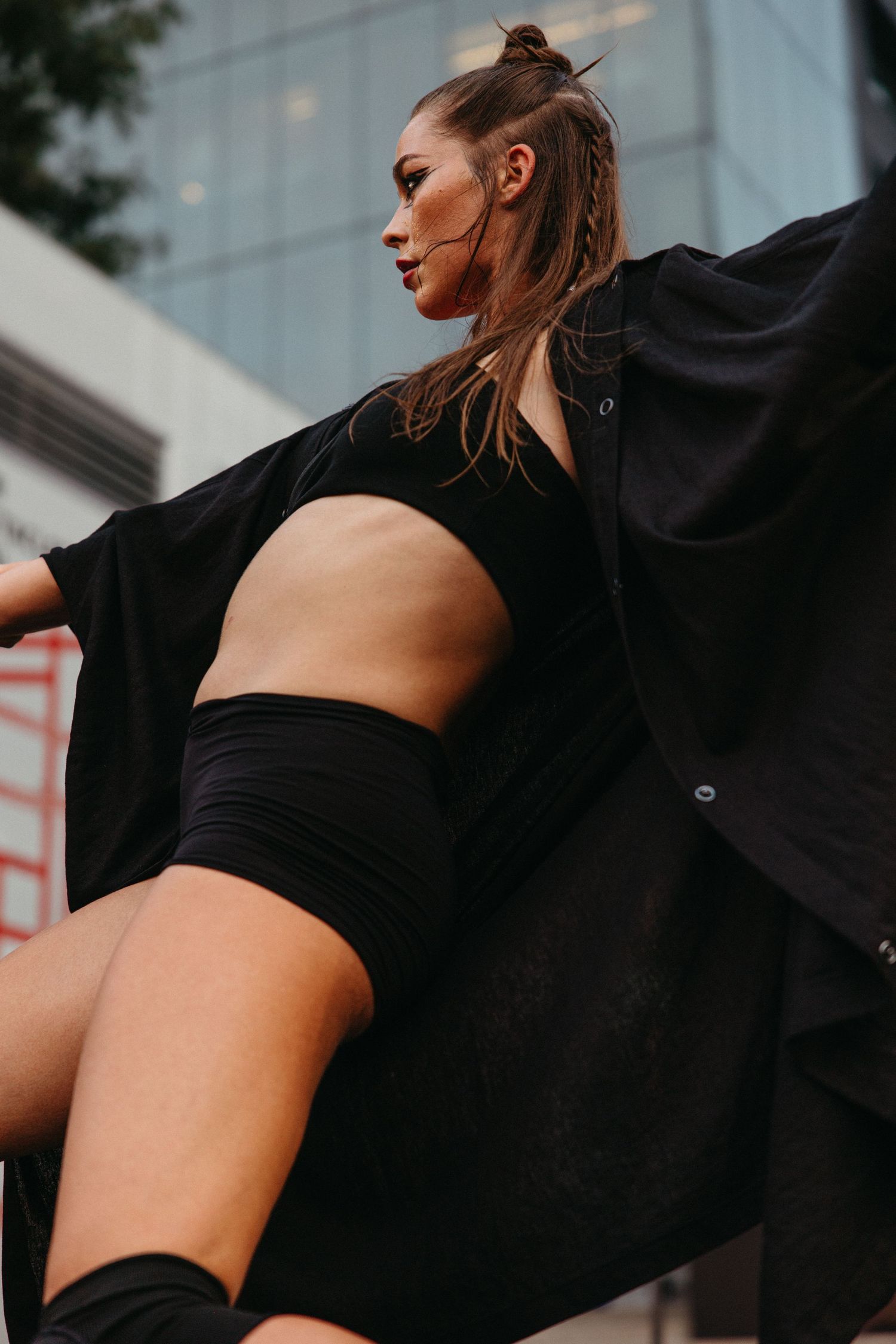 Athletic woman in black workout attire stretches gracefully against urban backdrop in dynamic photo series.