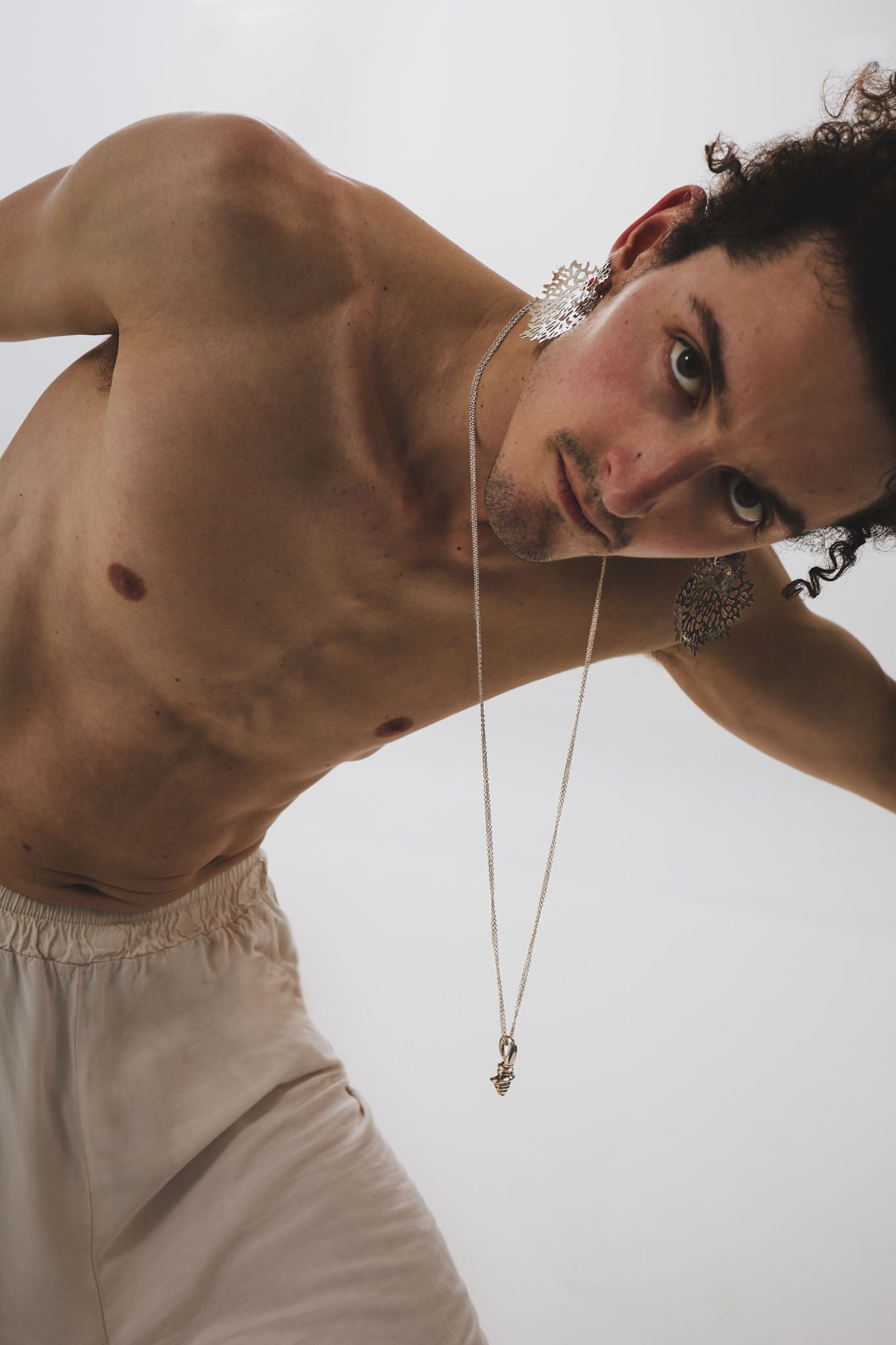 A portrait featuring dramatic lighting showcases a silver necklace against beige attire in an artistic pose.