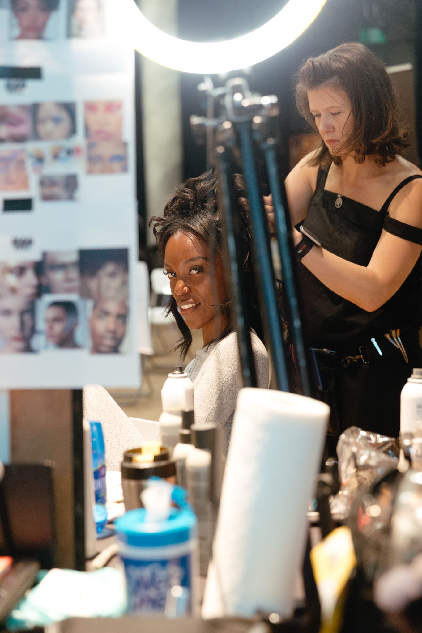 Behind the scenes photo of a busy makeup artist working in a professional studio setting with bright ring lights.