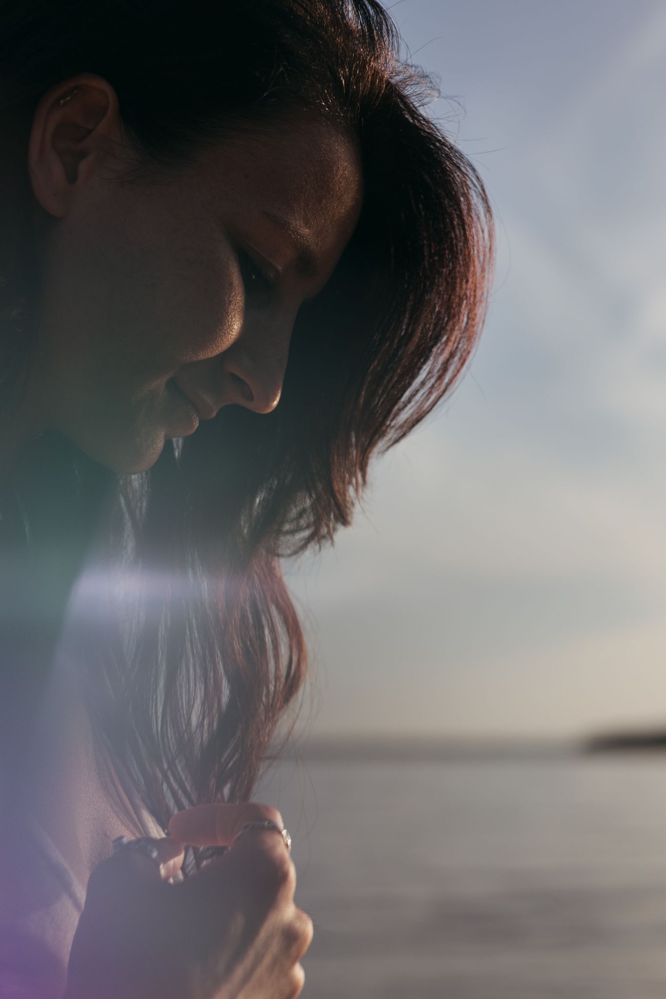 A silhouetted profile view against a hazy waterfront backdrop at dusk with soft natural lighting.