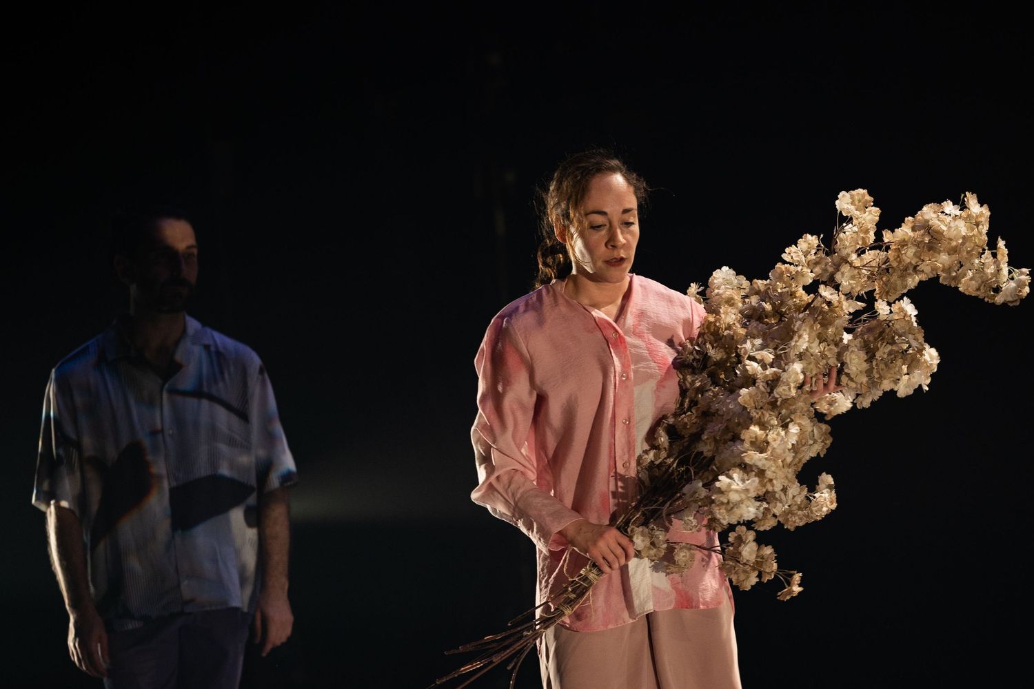 Person in pink attire exhaling smoke on dark stage while another figure stands in background.