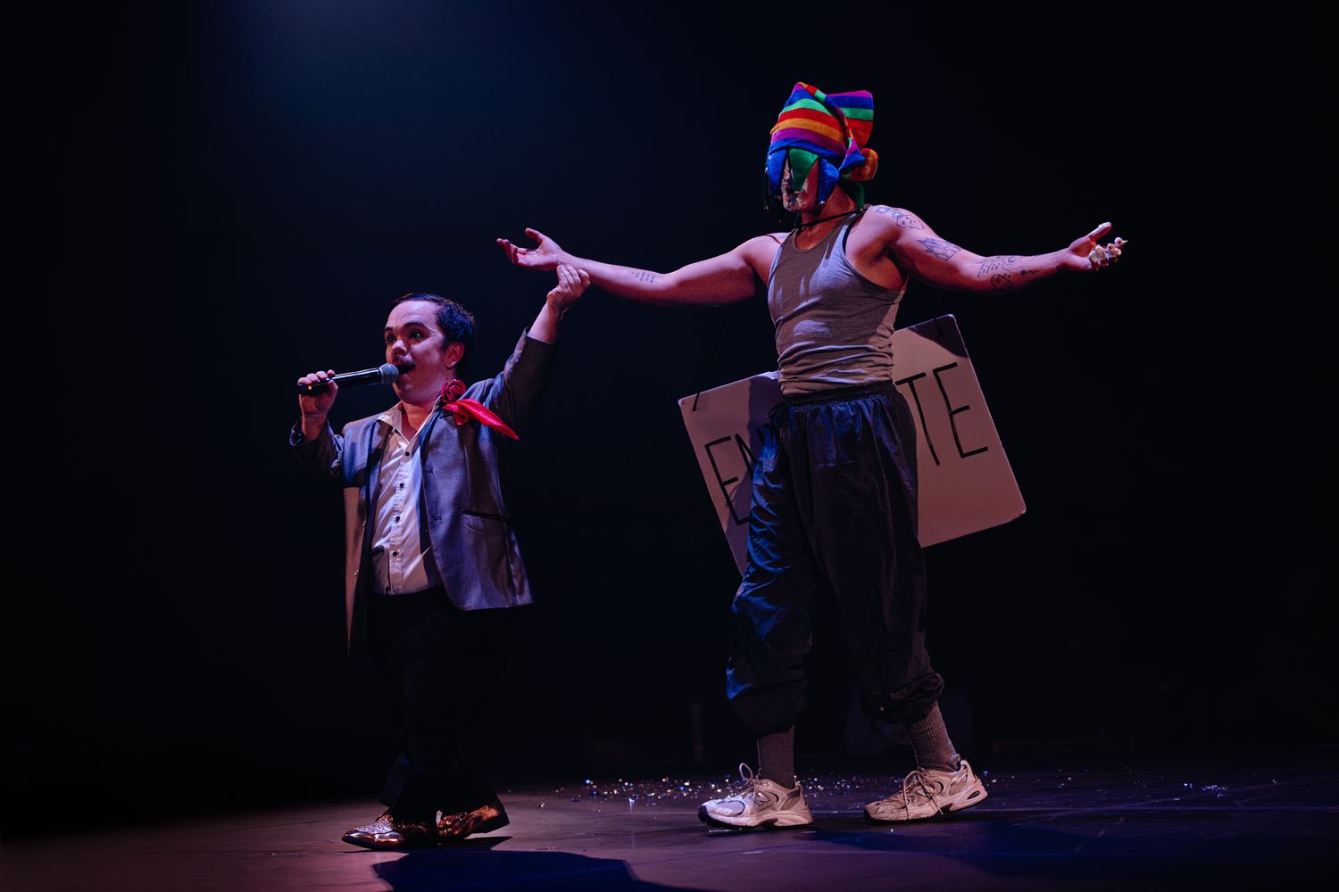 Performer in casual attire strikes dynamic pose during stage performance with dramatic lighting.