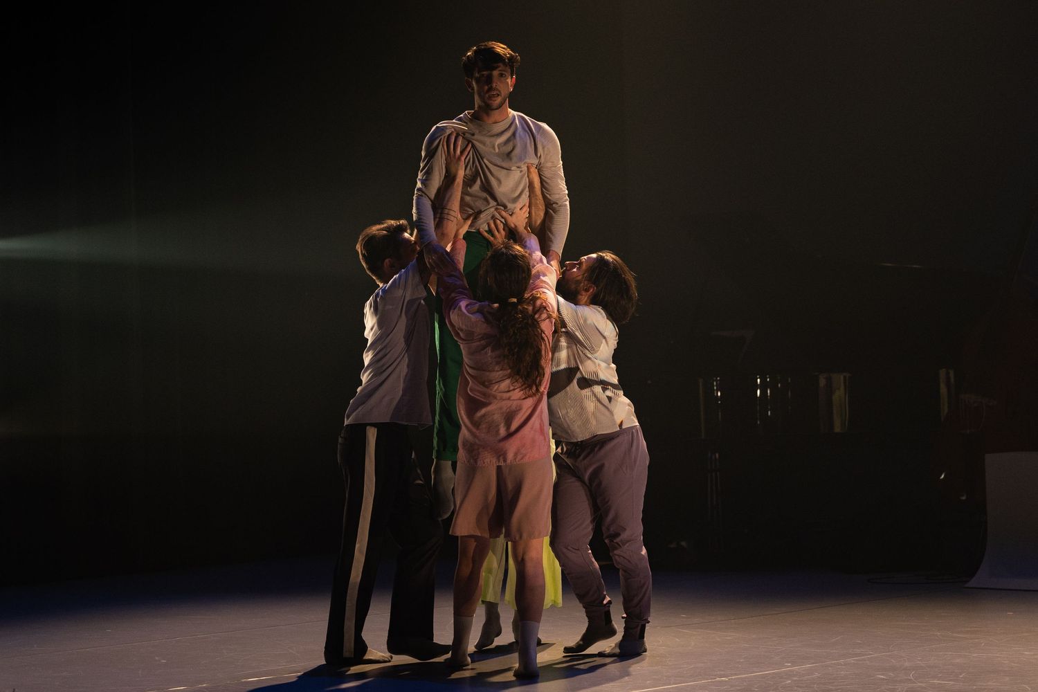 Six performers in dramatic theatrical scene on dark stage executing coordinated dance movements.
