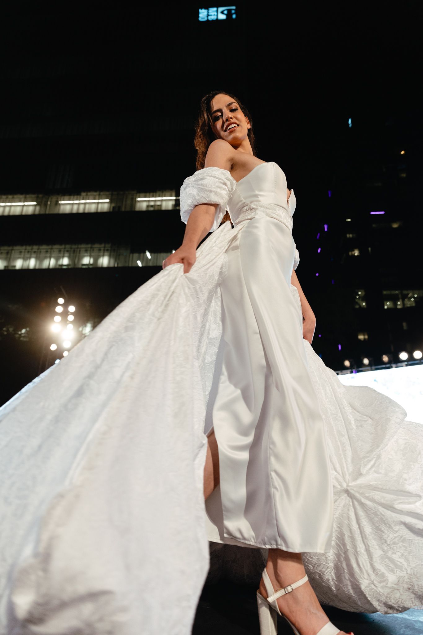 A flowing white dress twirls gracefully on stage during an evening performance with illuminated backdrop.