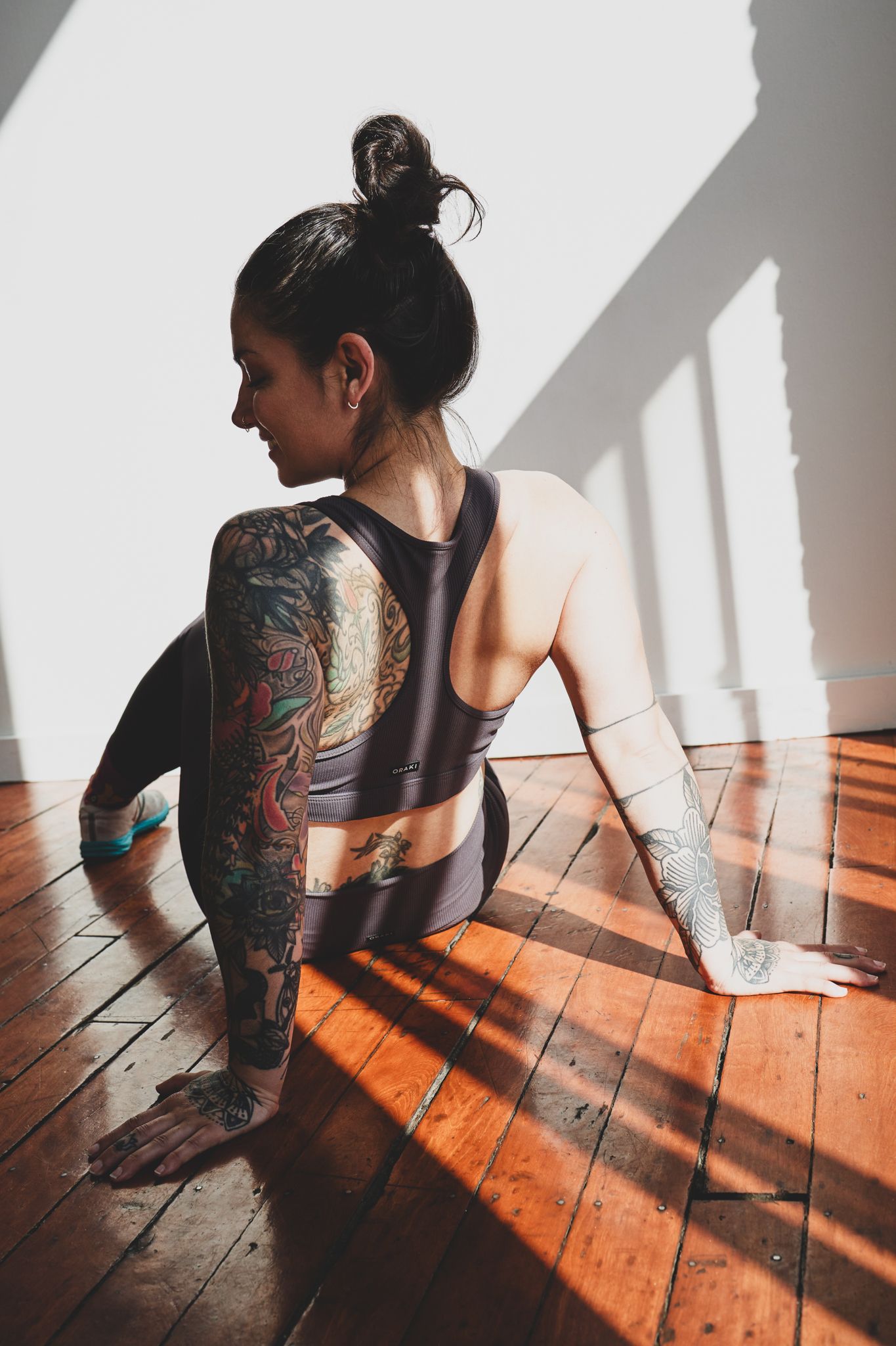 Artistic photograph showing a back tattoo on bare skin in dramatic sunlight and shadows on wooden floors.