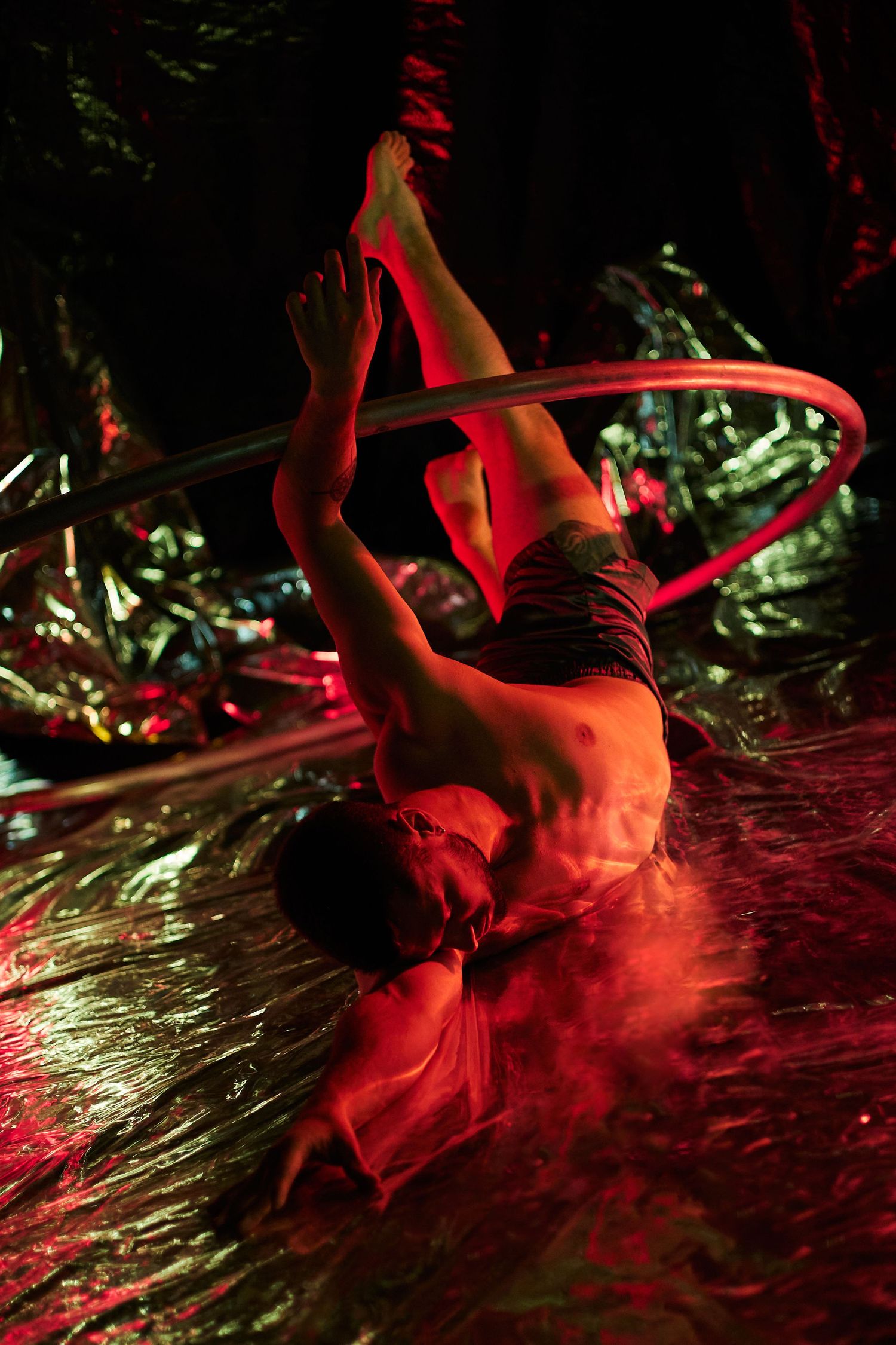 A performer in red lighting dances with a hoop on stage during an artistic circus performance.