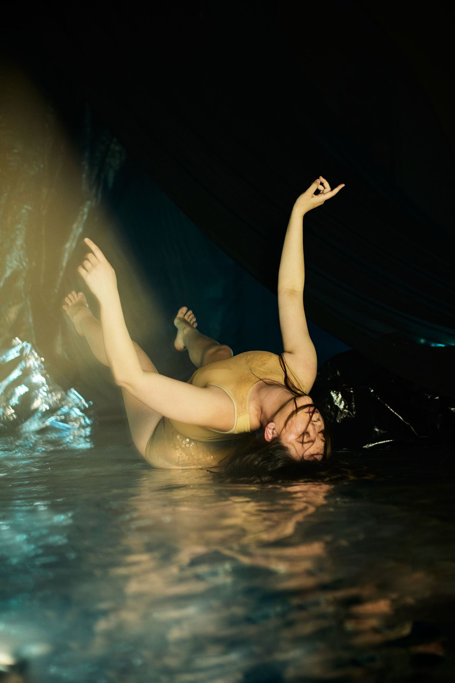 Figure floats gracefully in dark water with artistic dance-like movements illuminated by atmospheric lighting.
