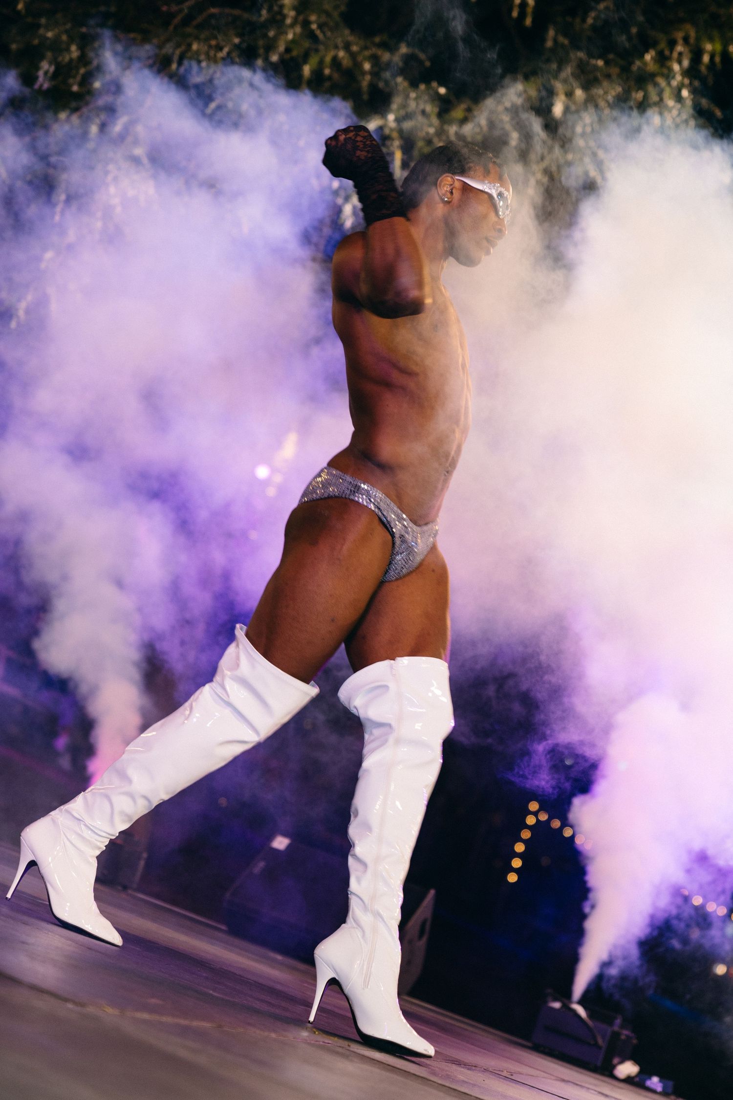 A performer in white boots dances on stage surrounded by dramatic purple smoke effects during a dynamic performance.