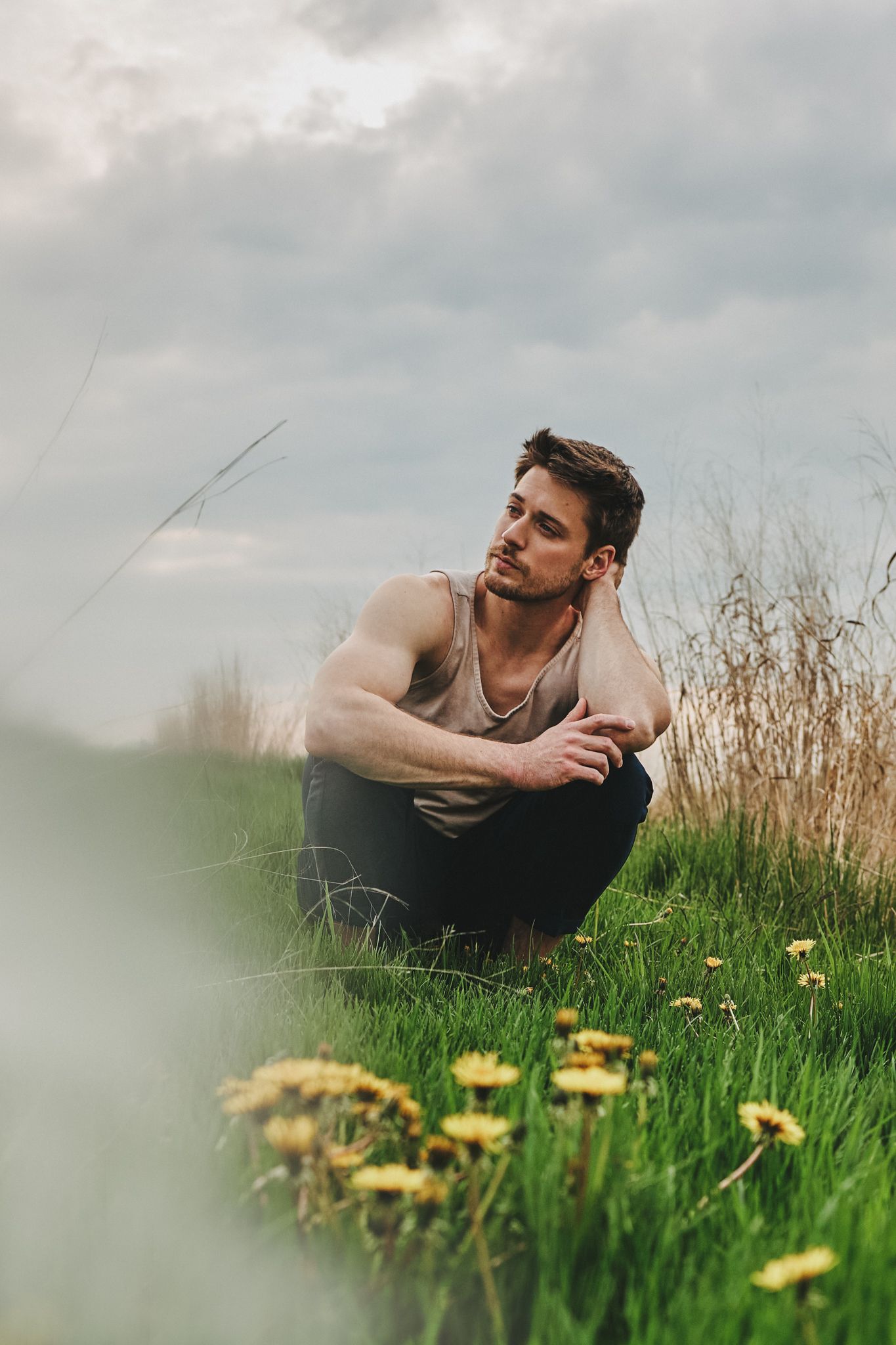 A person sits contemplatively among yellow wildflowers in a grassy field on an overcast day.