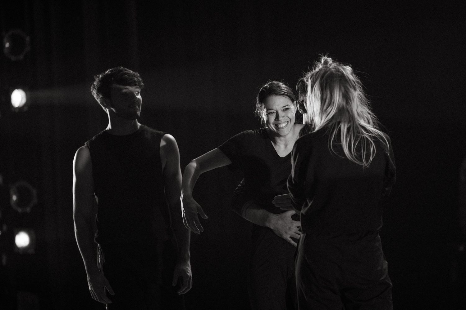 Black and white photograph showing three performers on a dark stage lit by dramatic spotlighting.