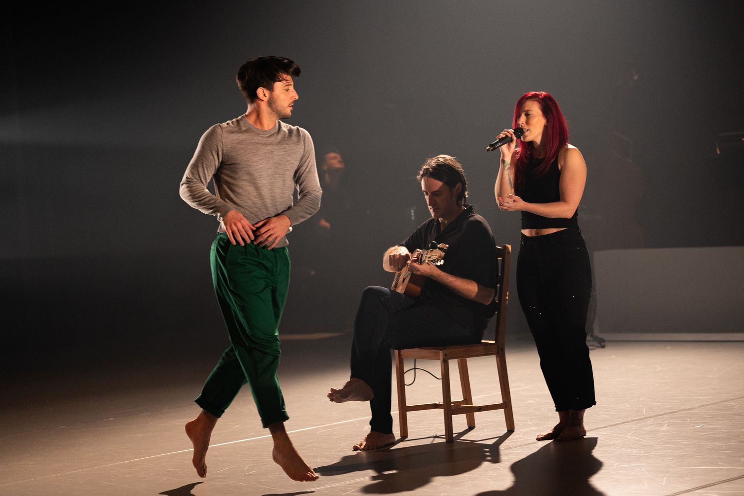 A dramatic dance performance sequence showing two performers moving together in a dimly lit studio space.
