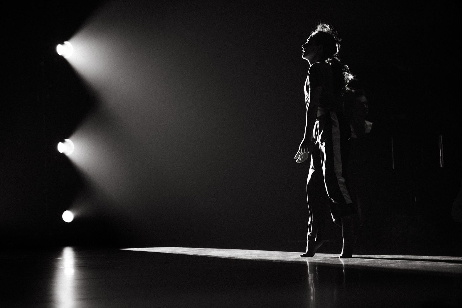 Silhouetted figure performs dramatic dance moves against stark black and white lighting on stage.