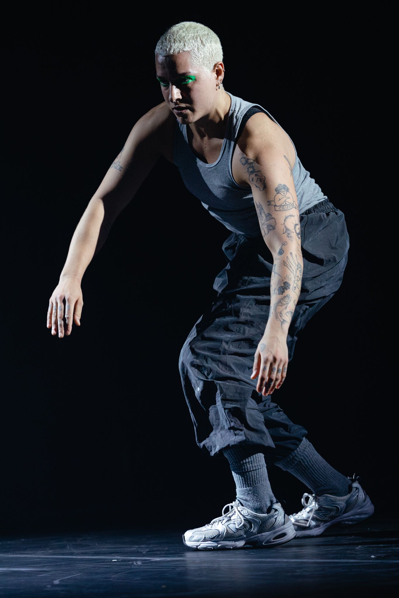 Dancer in athletic wear and sneakers performs modern dance move against black backdrop with dramatic lighting.