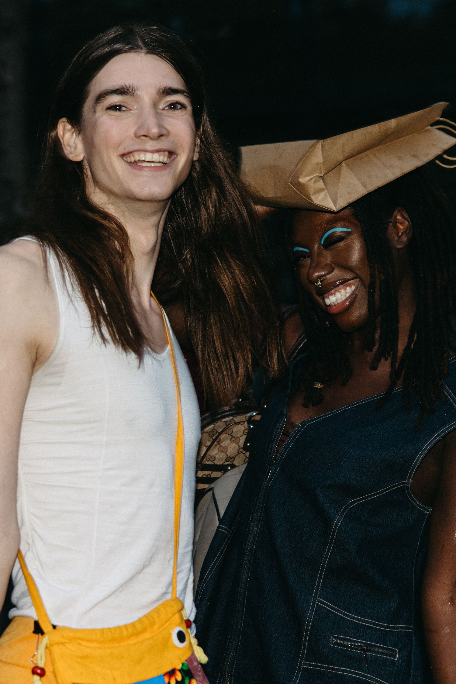 Two friends share a joyful moment together, one wearing a white tank top and yellow pants, the other in dark denim.