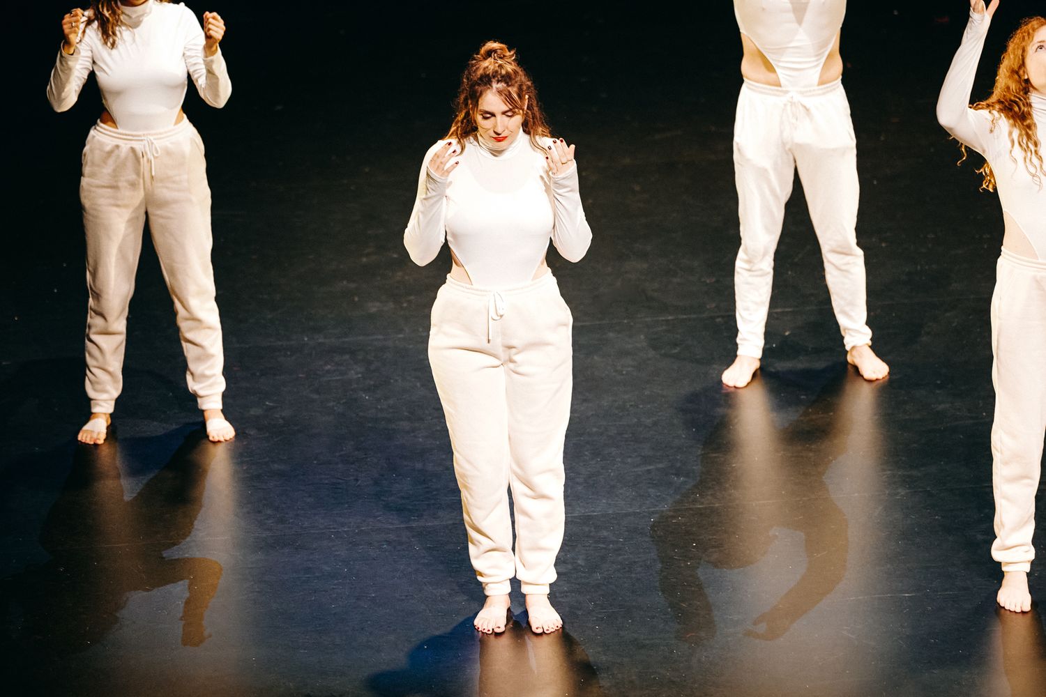 Dancers in all-white outfits perform on a dark stage during a contemporary dance piece.
