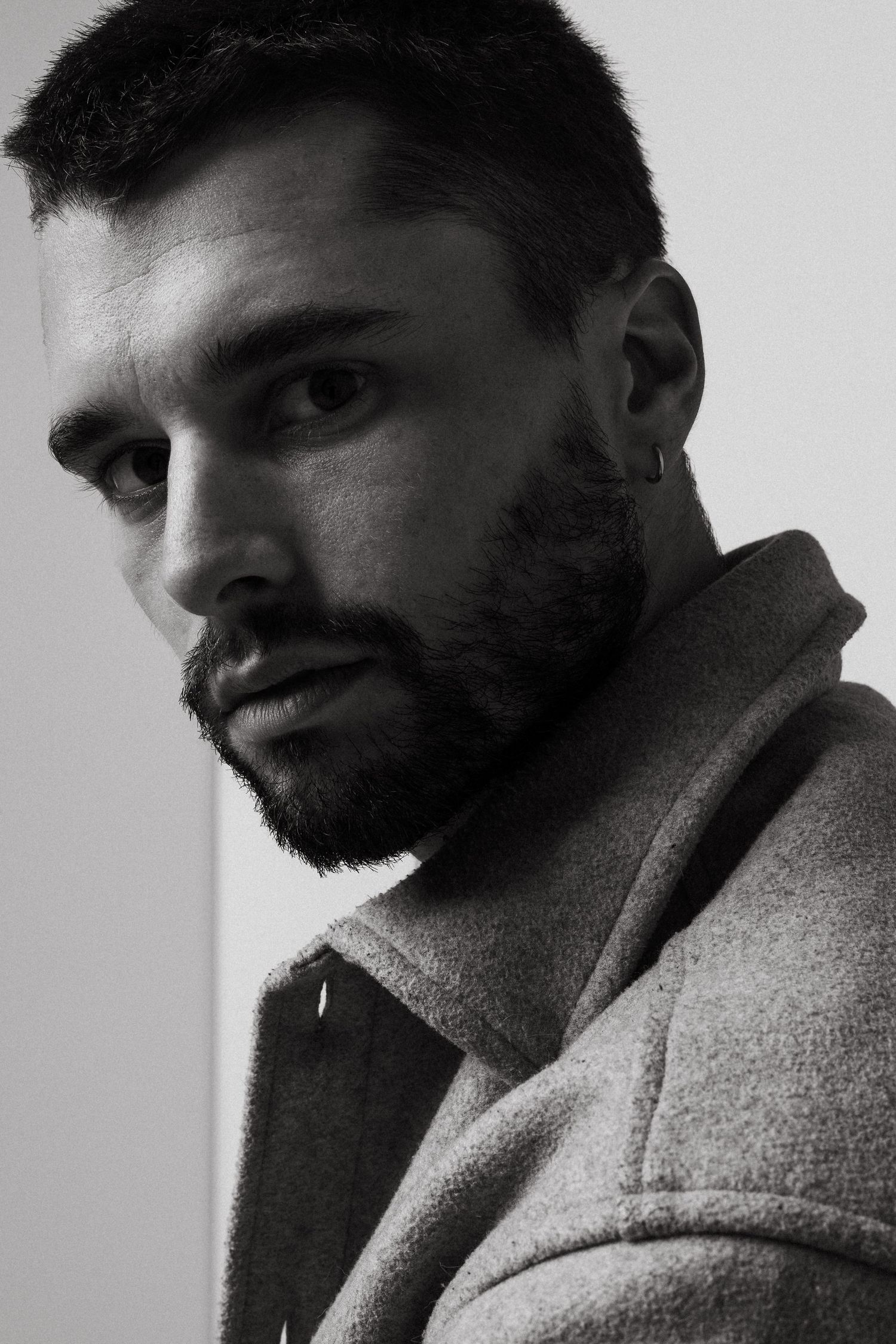 Dramatic black and white portrait of a bearded man in profile wearing a wool coat.