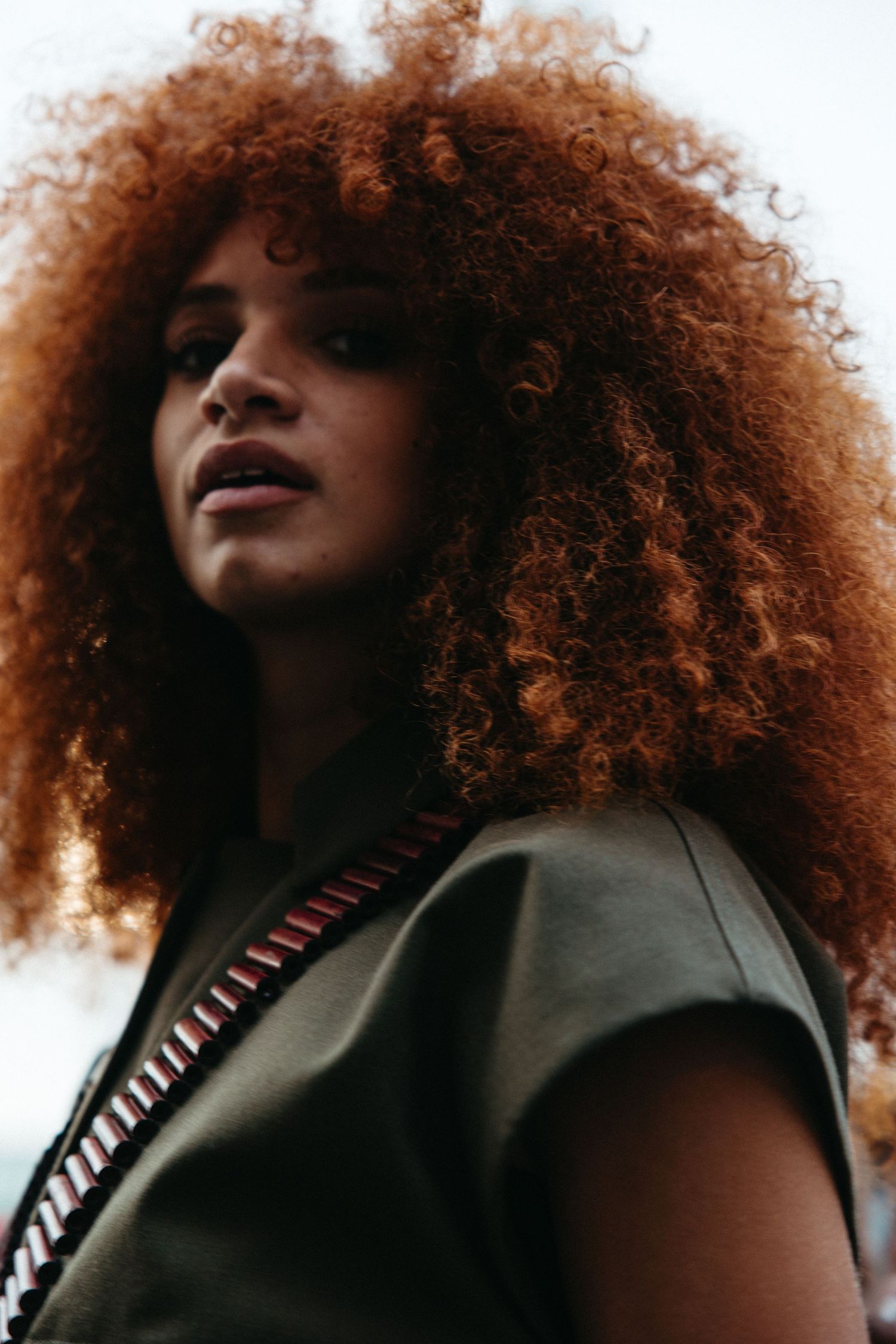 Dramatic portrait series showing curly red-brown natural hair and dark clothing against a light background.