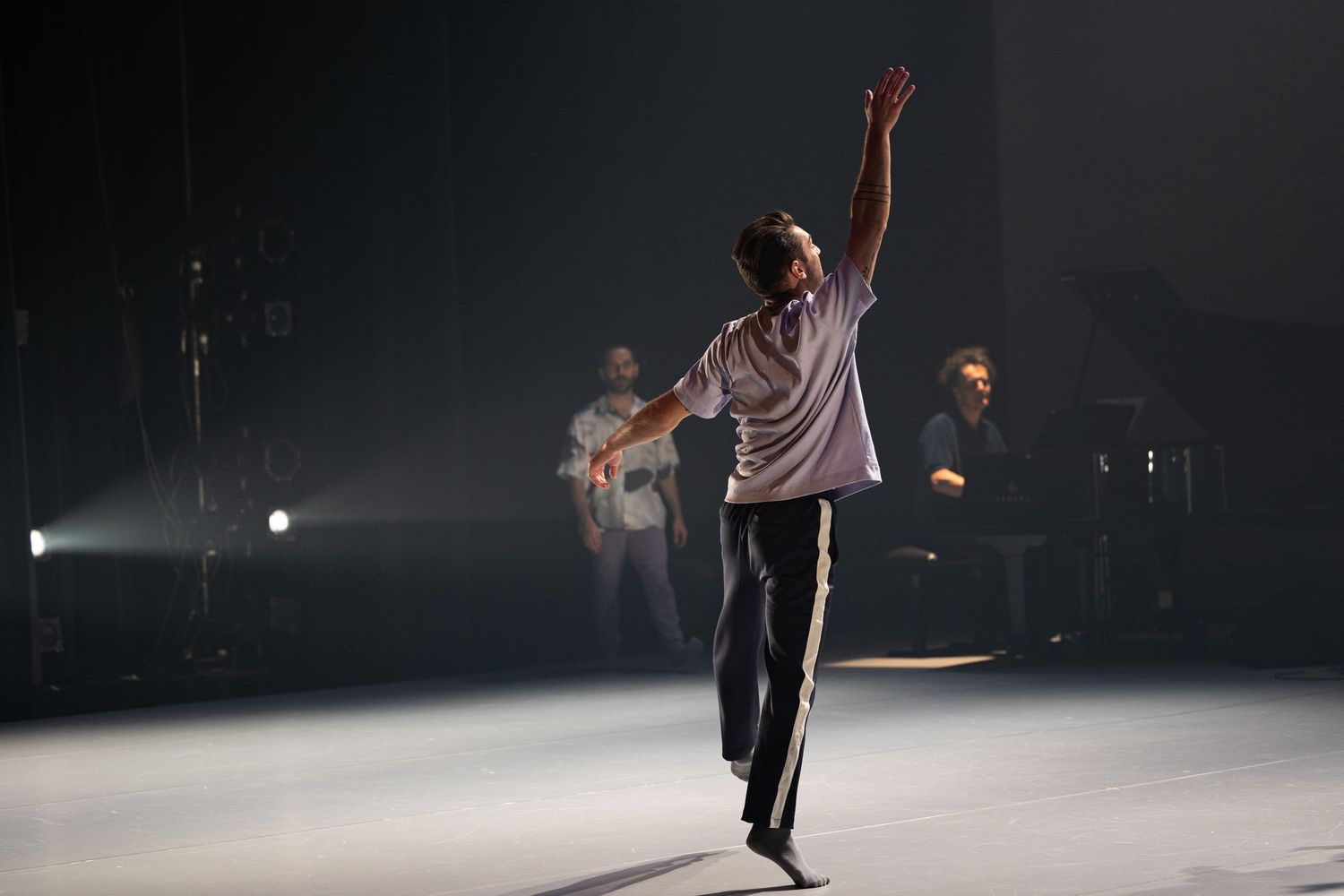 Single figure performs graceful dance moves on a dimly lit stage with atmospheric fog and spotlights.