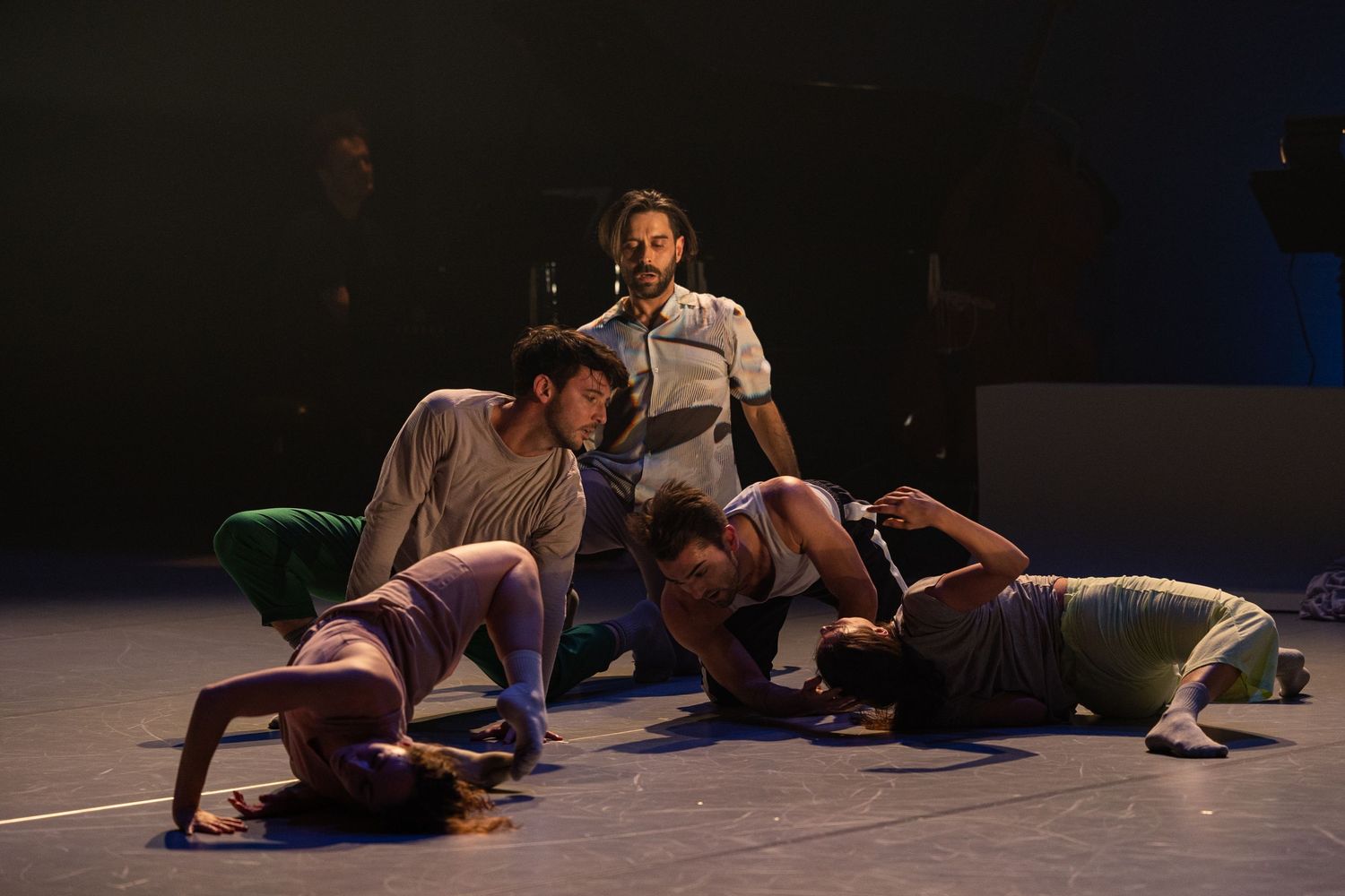 Contemporary dancers perform a dramatic floor sequence during a dance performance on a dark stage.