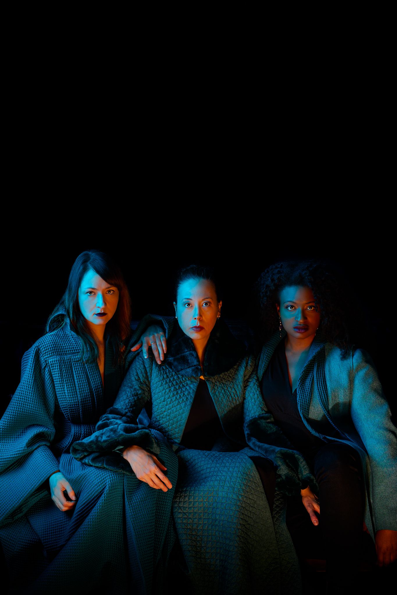A group sits together on a couch dramatically lit by blue and orange lighting in a dark room.