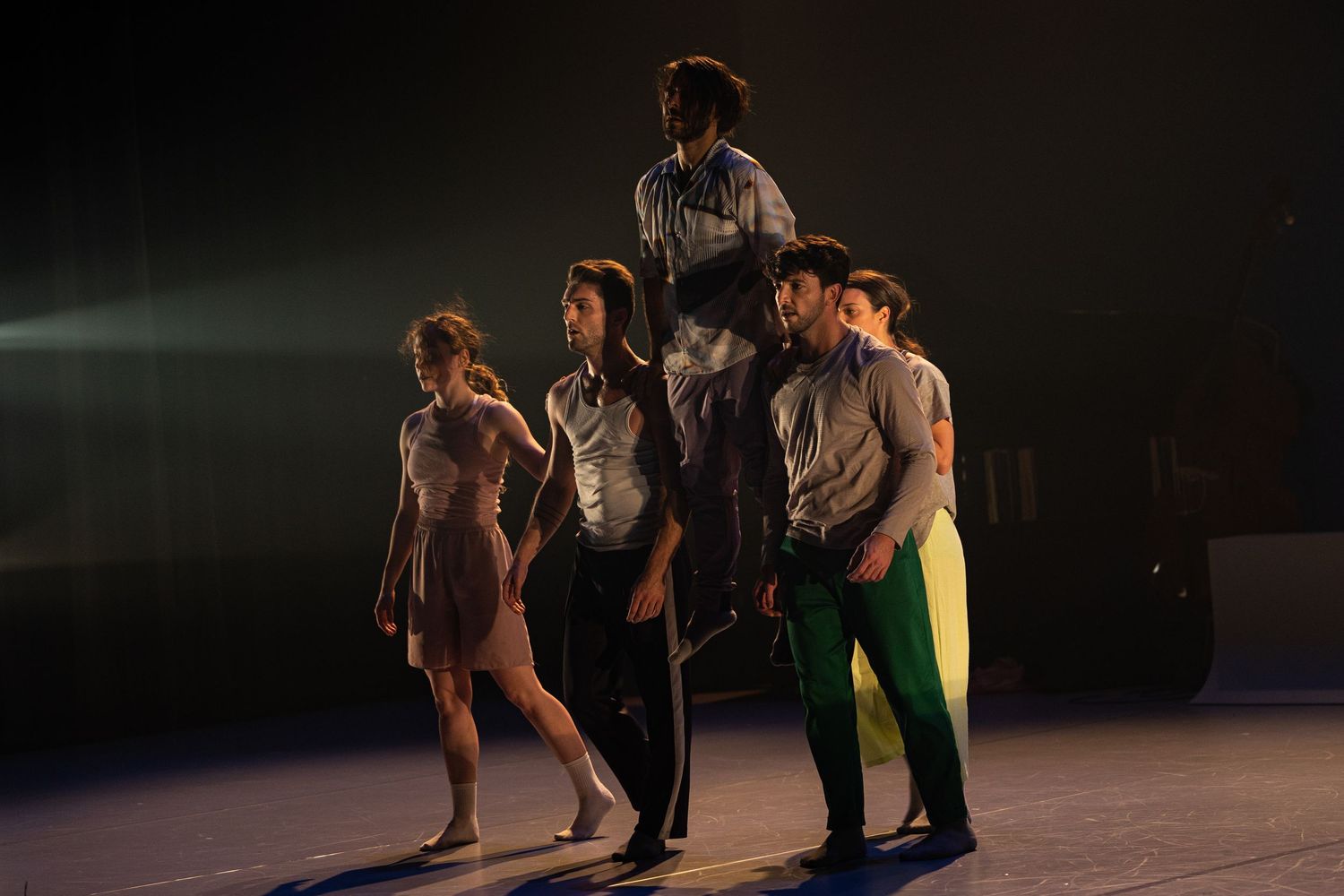 Dancers perform a contemporary dance piece on a dark stage with dramatic lighting and fluid movements.