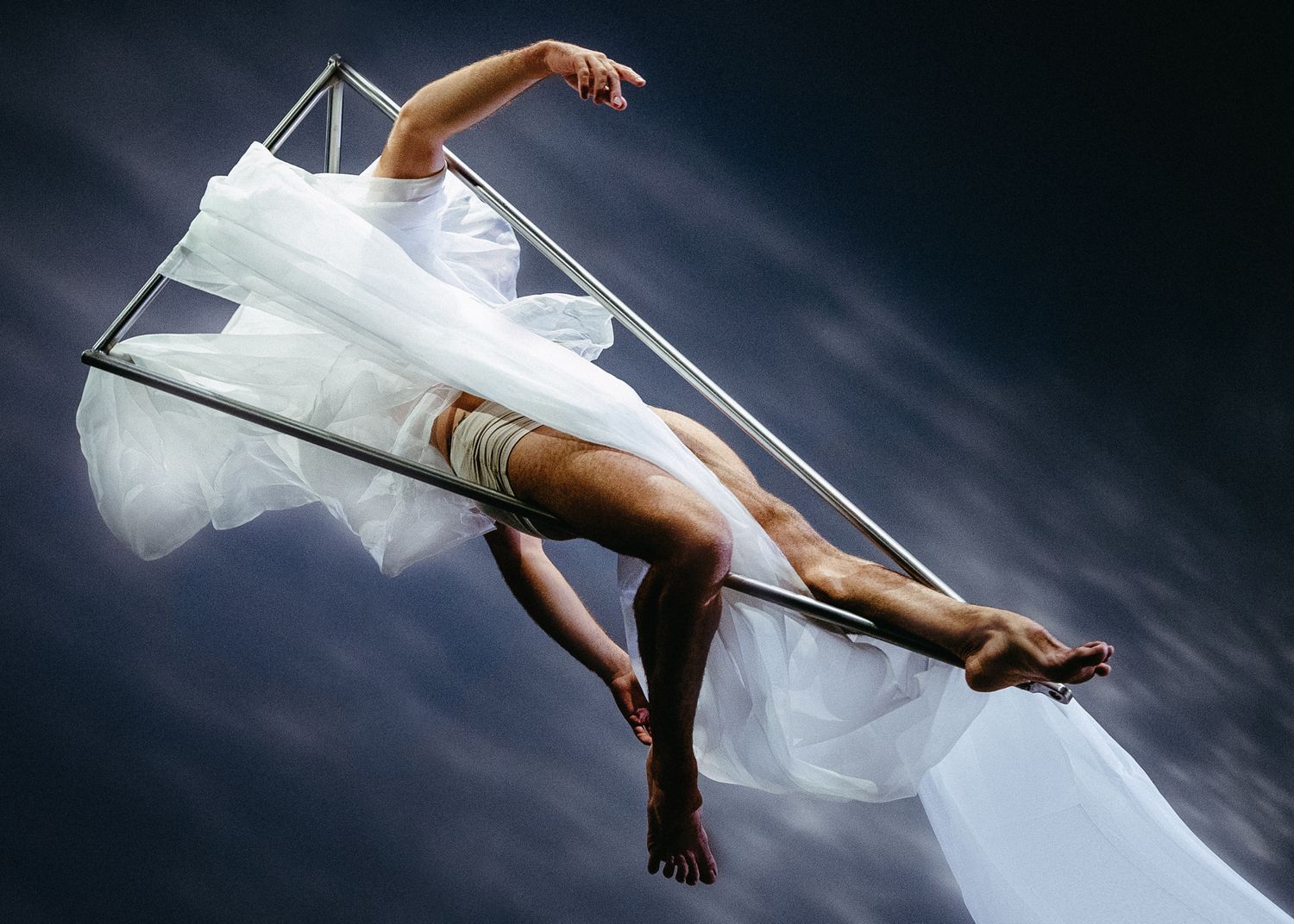 A dancer performs a dramatic pose with flowing white fabric against a dark background.