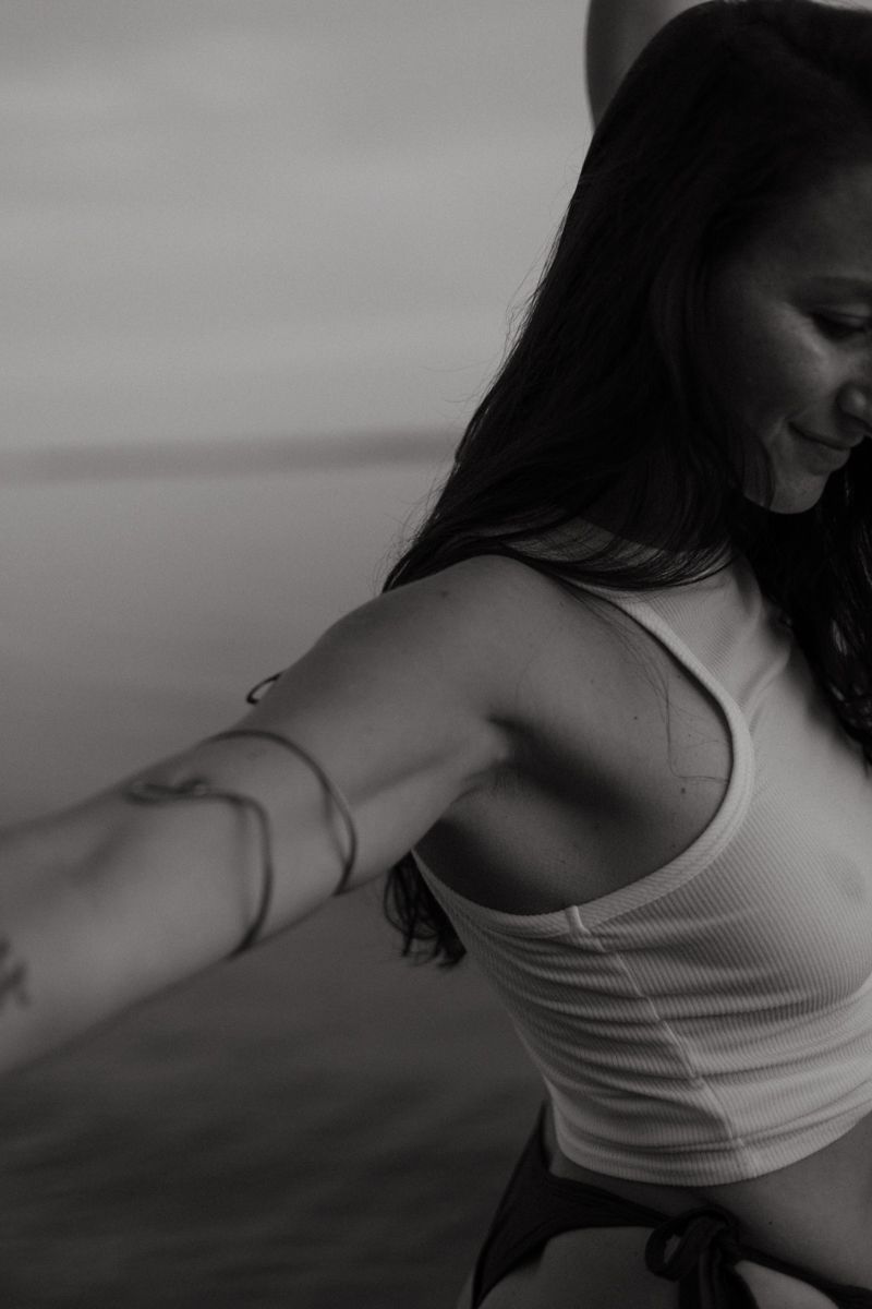 Black and white photo of person in white tank top with outstretched arm and dark hair against blurred background.