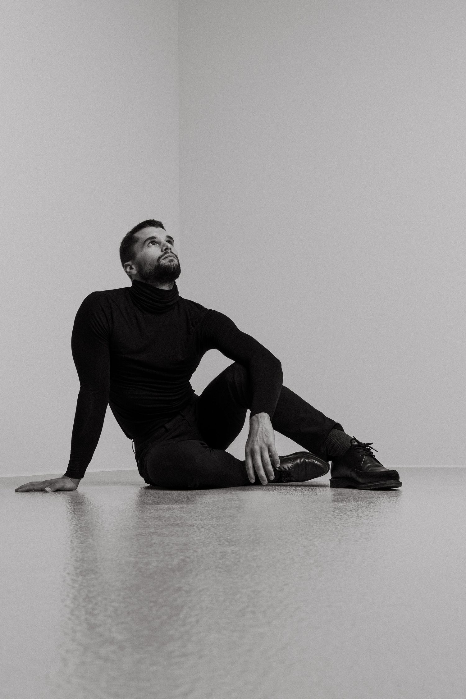 A person in black clothing lies on a white floor in three artistic black and white compositions.