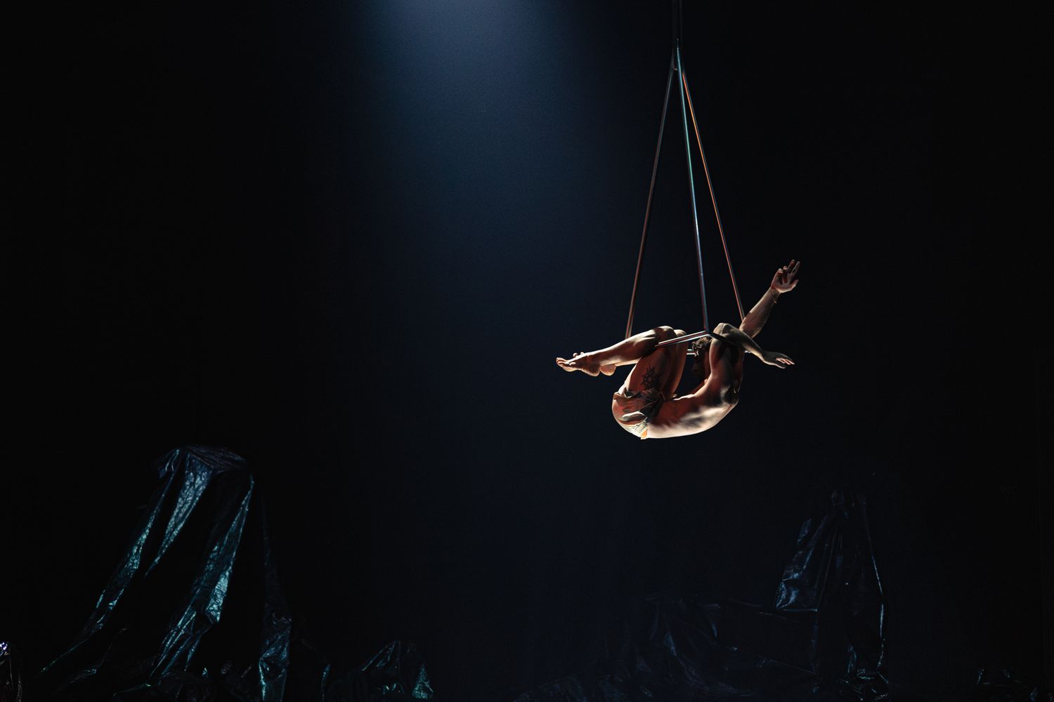 Aerial acrobat performers create a dramatic silhouette as they soar through the dark space in a captivating circus act.
