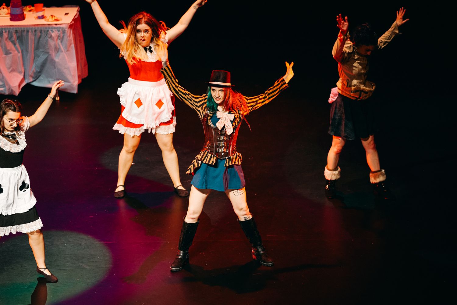 Performers in colorful costumes dancing energetically on a dark stage during a theatrical performance.