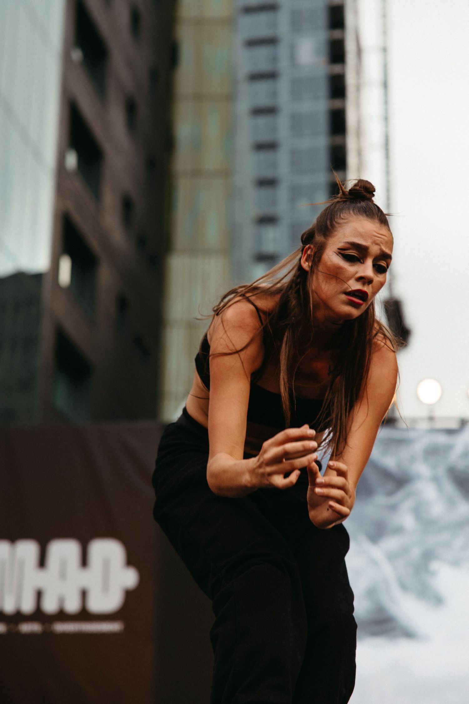 Dancer in black dress performs dramatic expressive movements in an outdoor urban setting.